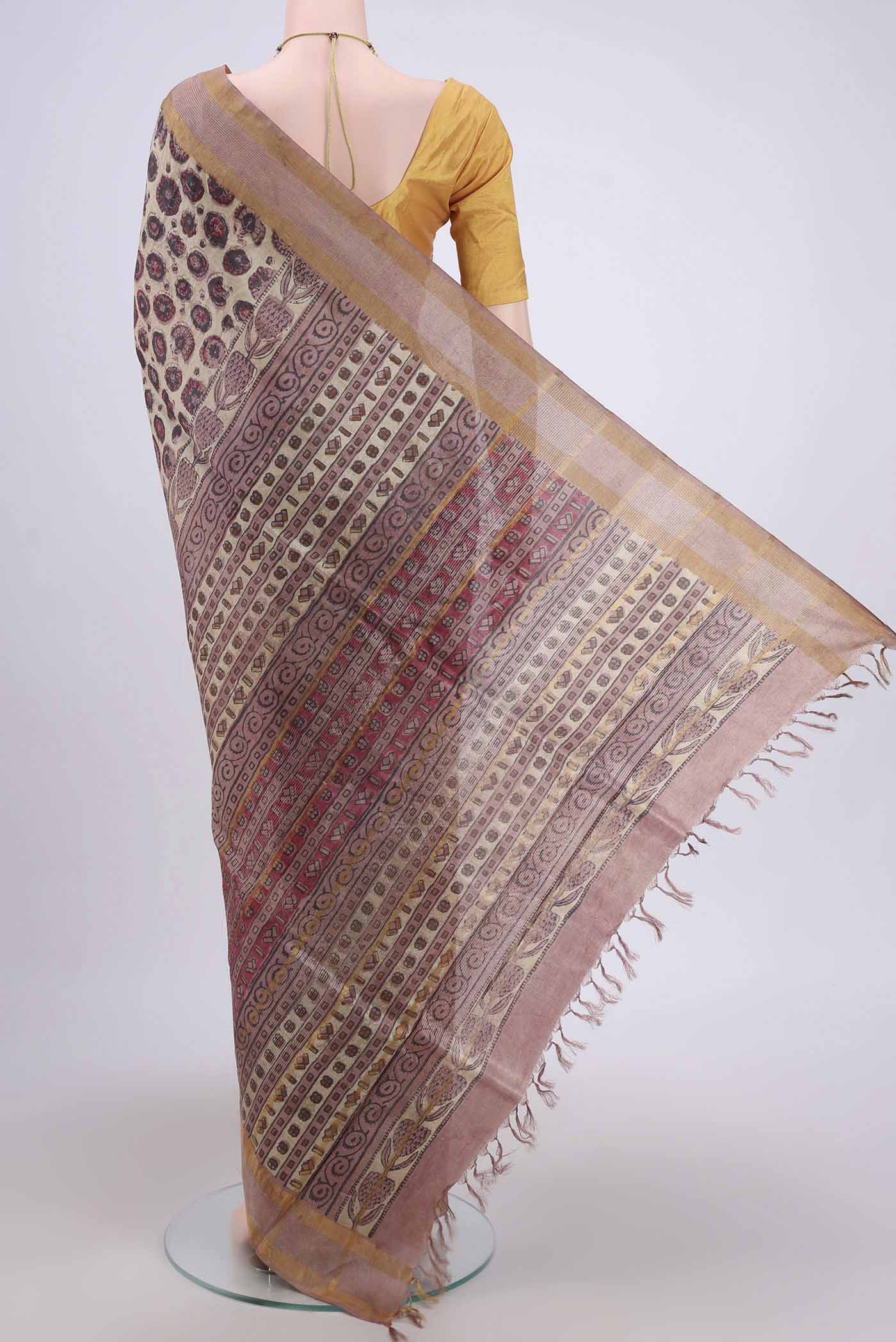 Flat view of Beige Tussar Silk Saree with kalamkari Print on the body and Zari Border. 