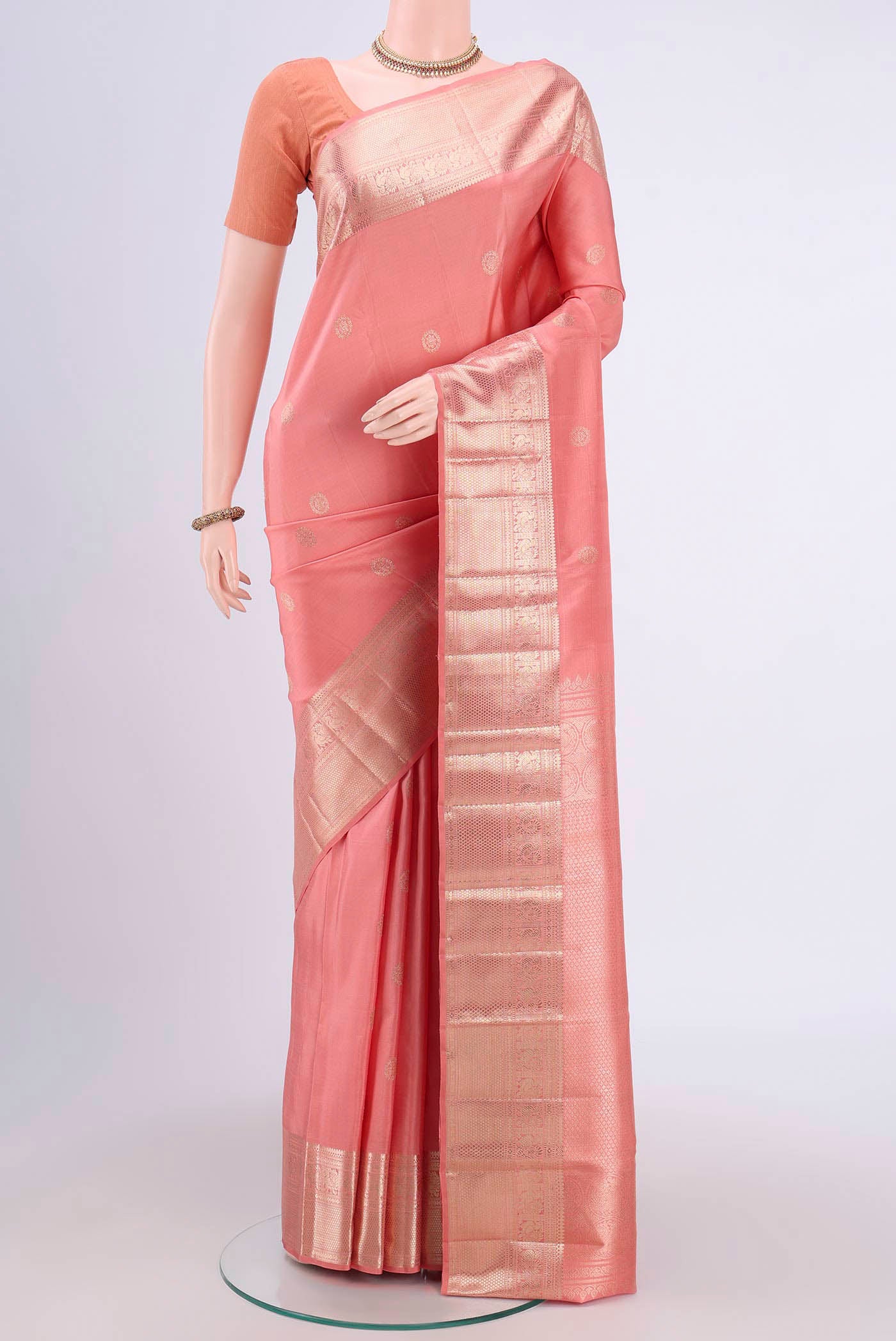 Peach Kanjivaram Saree with Zari Butta on the body and Zari Border.  displayed on a mannequin