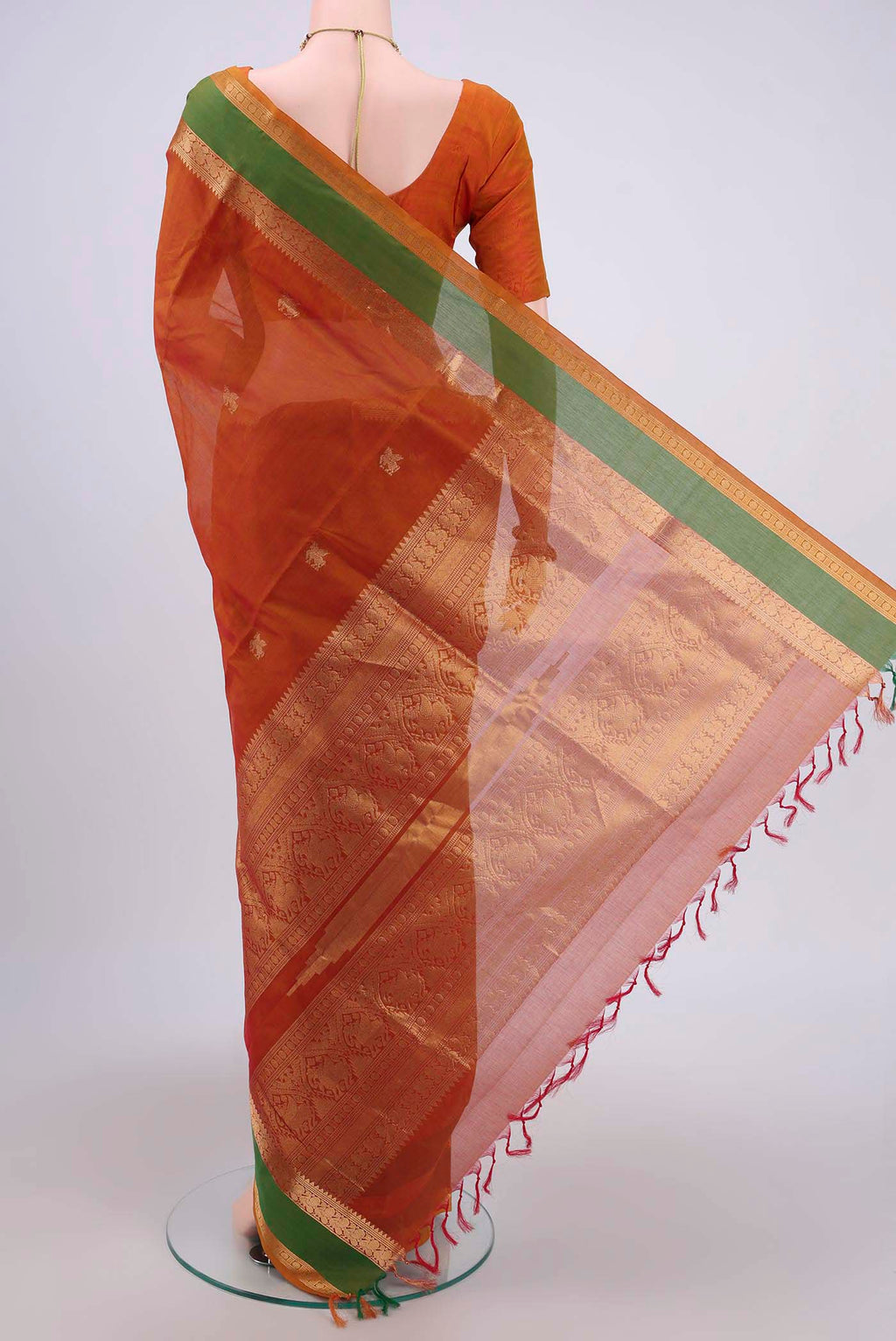 Flat view of Rust Silk Cotton Saree with Zari Butta on the body and Zari Border. 