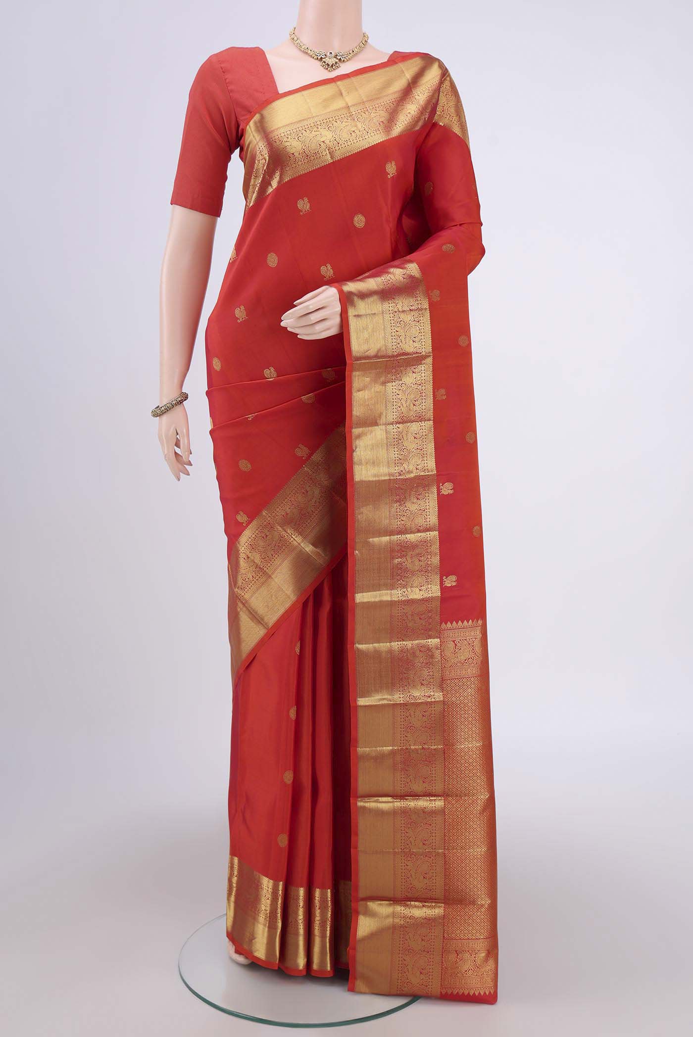 Orange Kanchipuram Silk Saree with Zari Butta on the body and Zari Border.  displayed on a mannequin