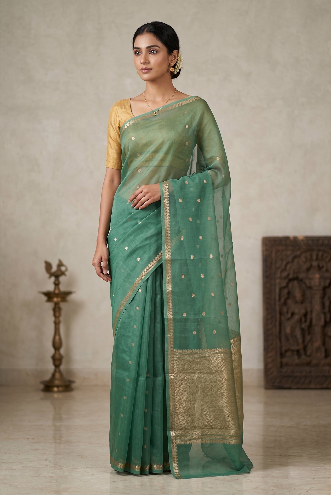 Model wearing a Turquoise Organza Silk Saree with Zari Butta on the body and Zari Border.