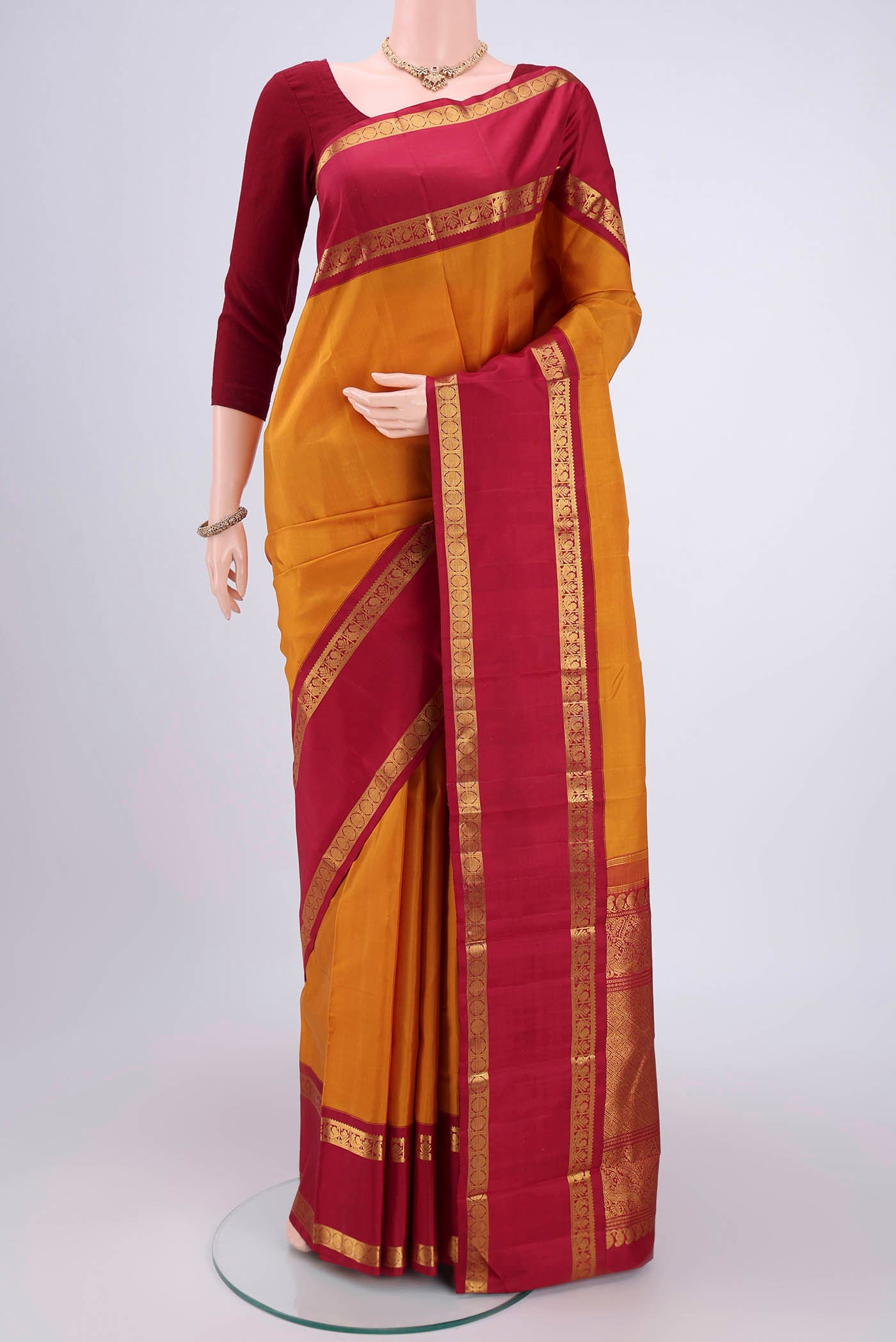 Mustard Kanchipuram Silk Saree with Plain Body and Zari Border.  displayed on a mannequin