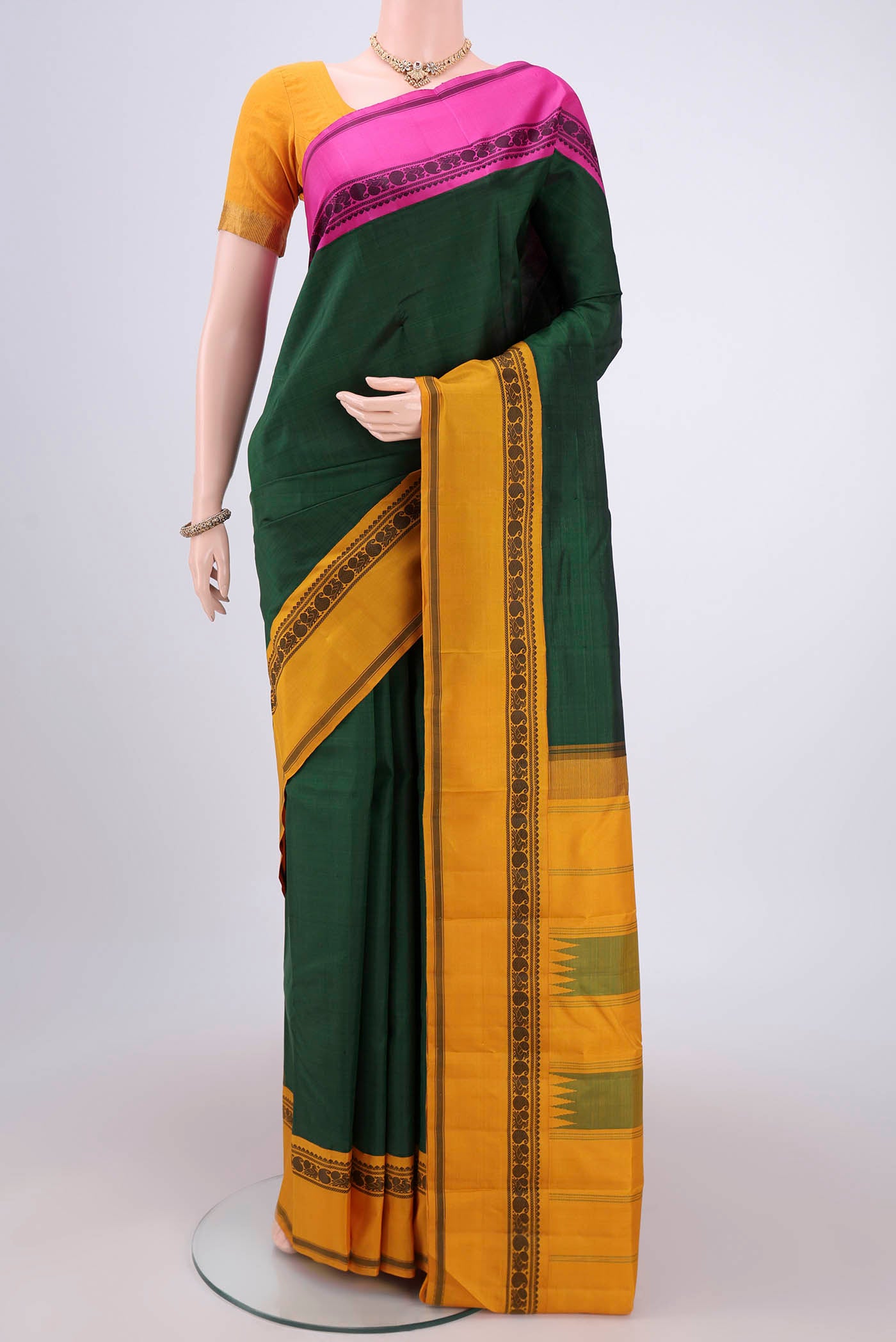 Bottle Green Kanjivaram Silk Saree with Plain Body and Ganga Jamuna Border.  displayed on a mannequin