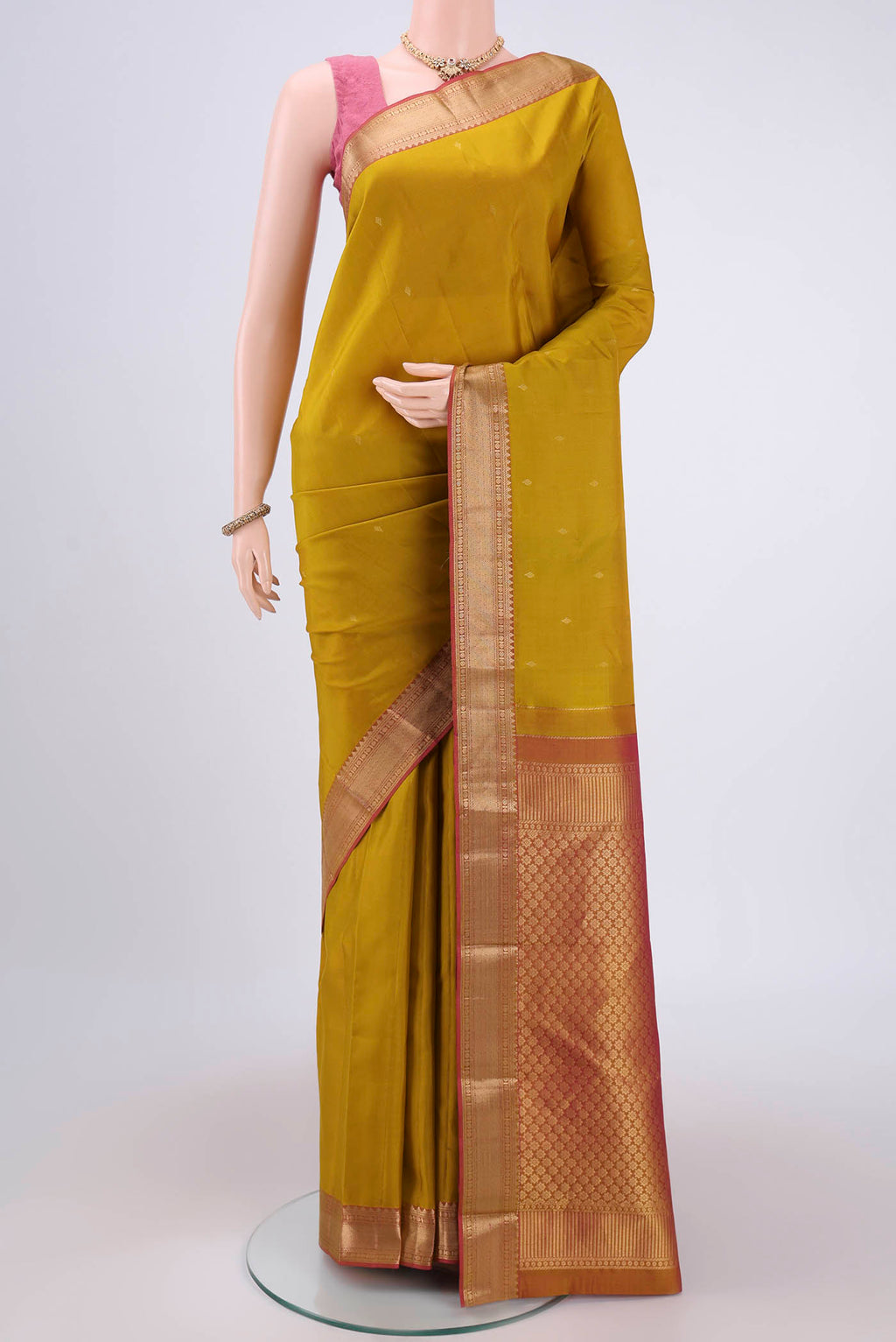 Mustard Kanchipuram Silk Saree with Zari Butta on the body and Zari Border.  displayed on a mannequin