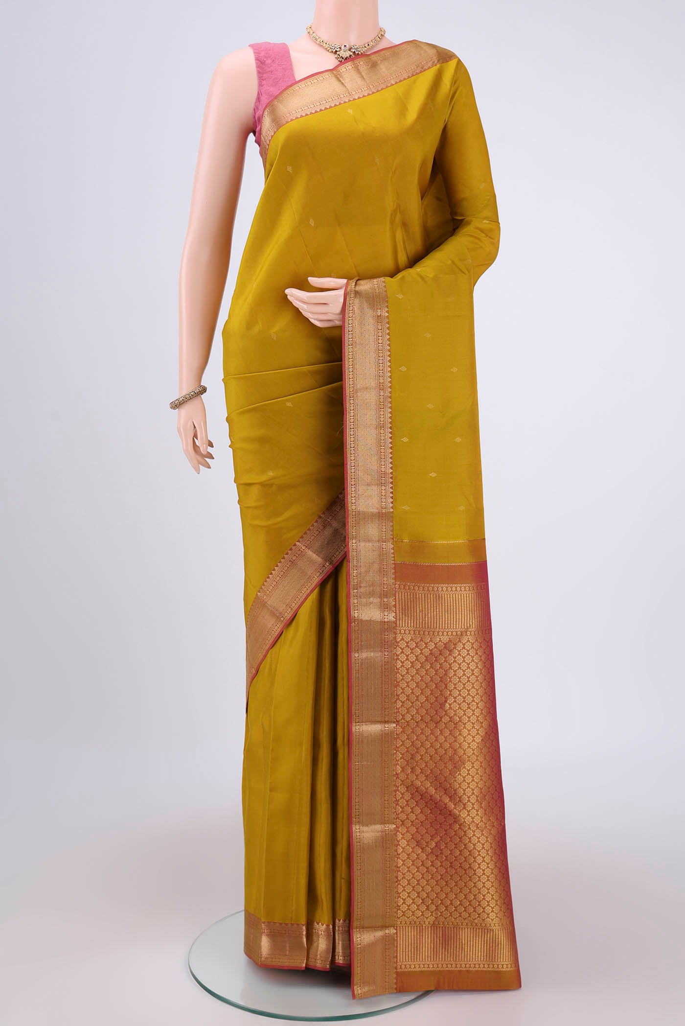 Mustard Kanchipuram Silk Saree with Zari Butta on the body and Zari Border.  displayed on a mannequin
