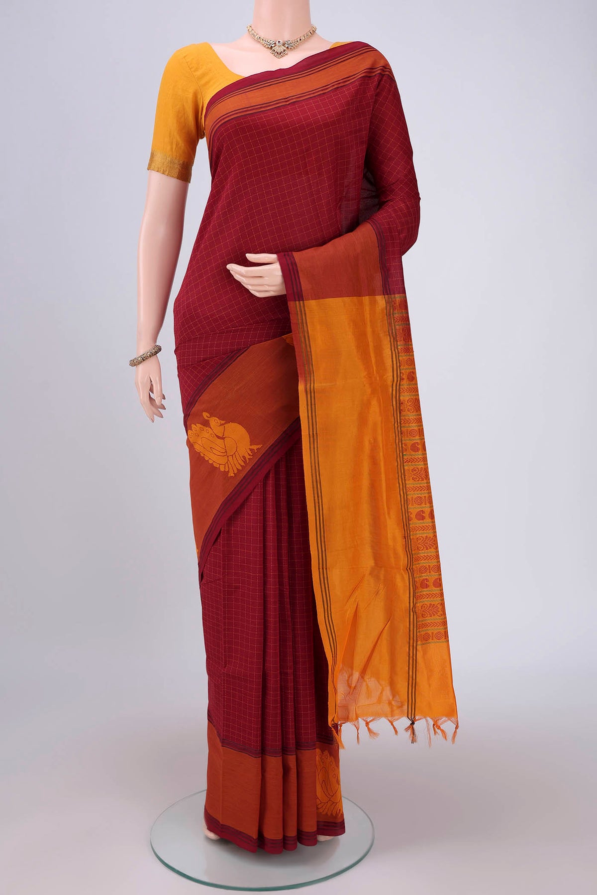 Maroon Blended Poly Cotton Saree with Checked design on the body and Thread Border.  displayed on a mannequin