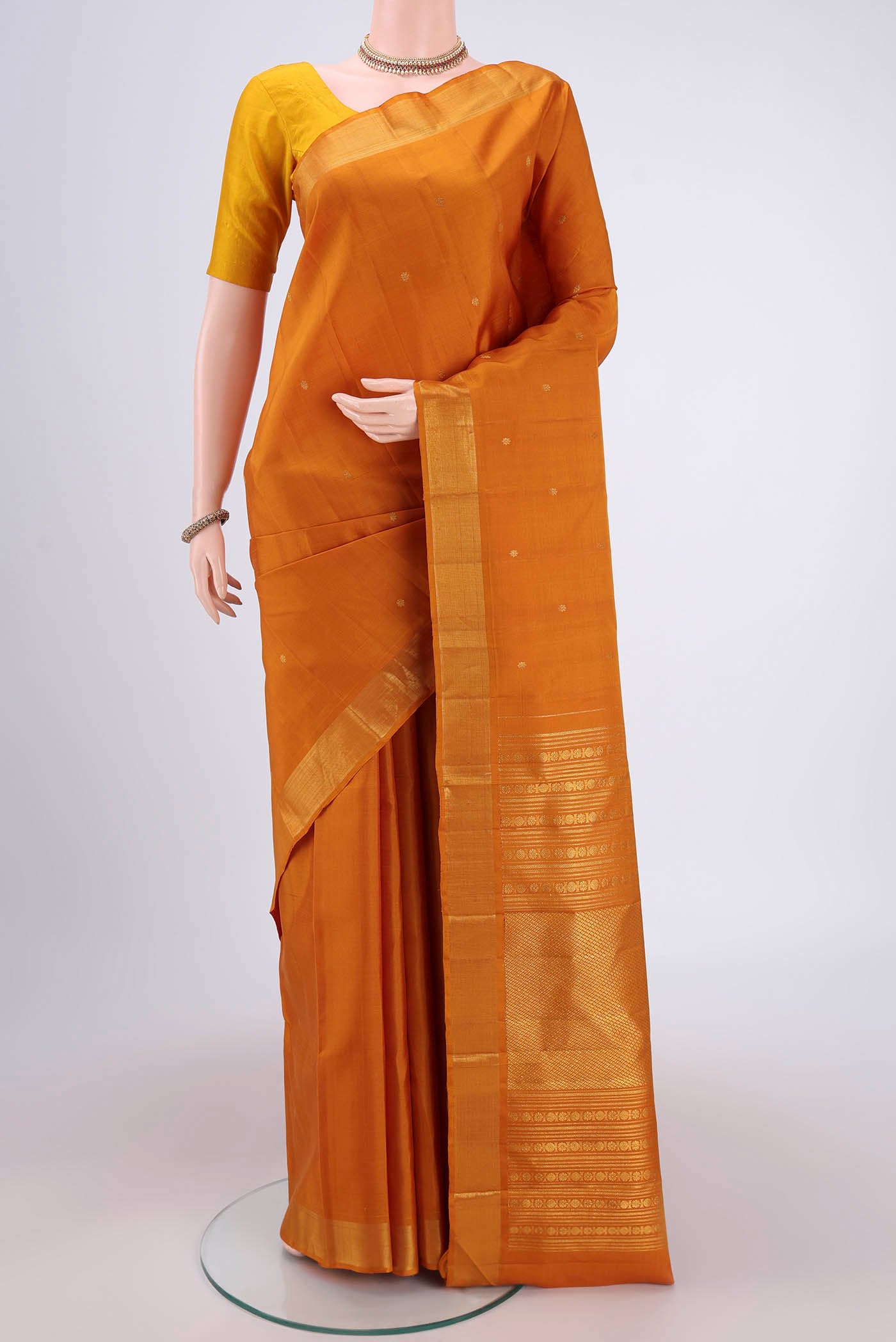 Mustard Kanjivaram Silk Saree with Zari Butta on the body and Zari Border.  displayed on a mannequin