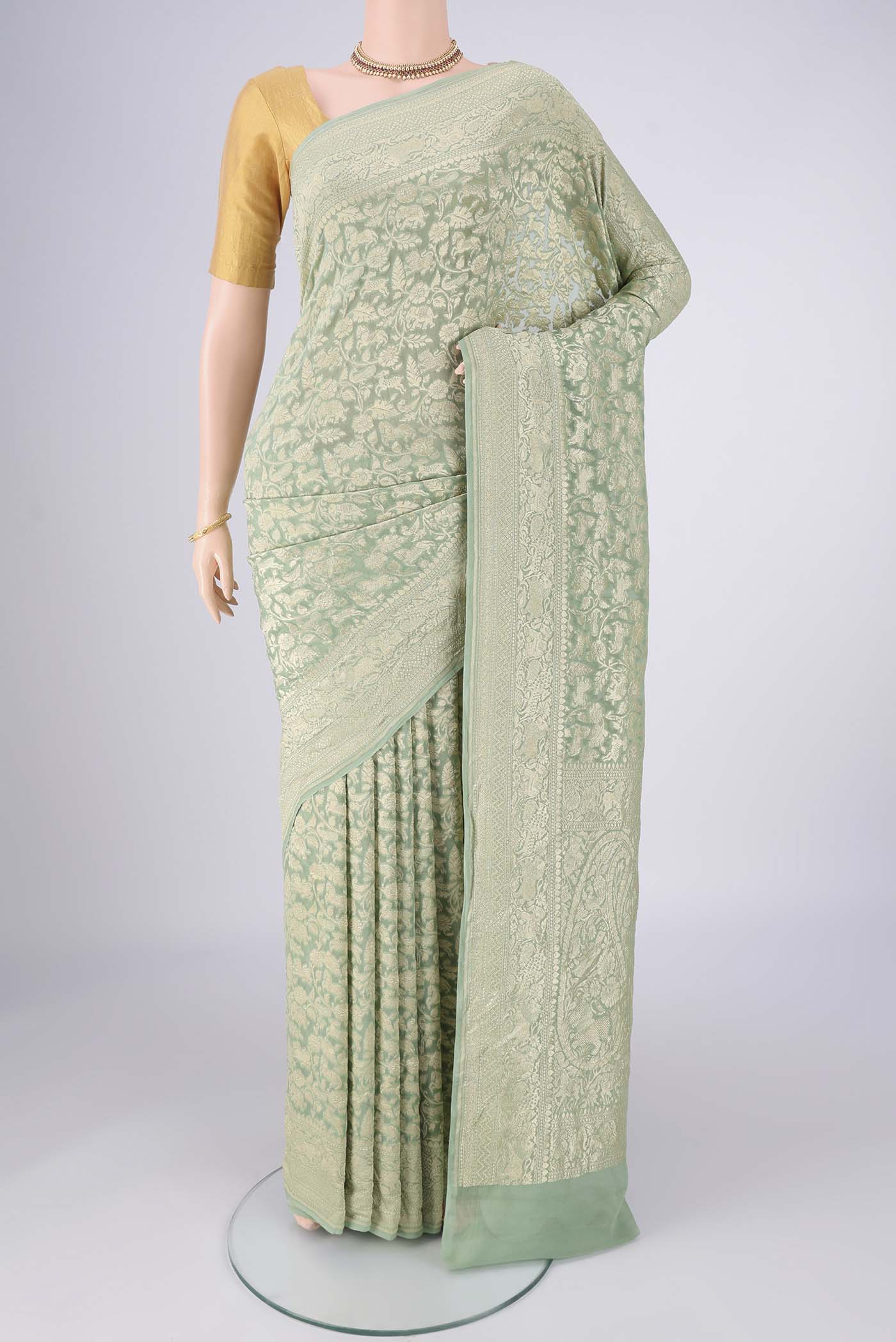Sage Green Banarasi Georgette Saree with Zari Brocade on the body and Zari Border.  displayed on a mannequin