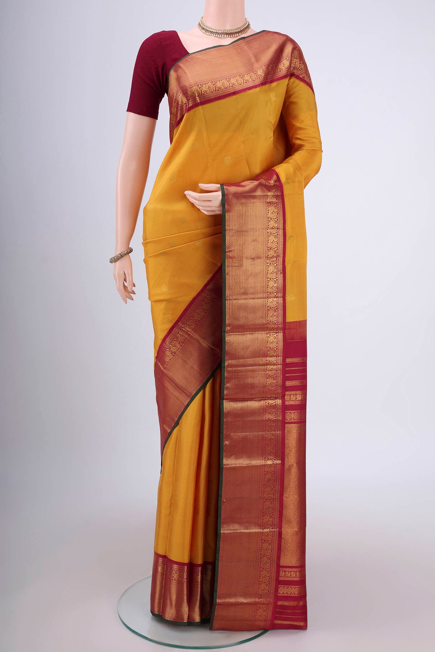 Mustard Kanjivaram Silk Saree with Zari Butta on the body and Zari Border.  displayed on a mannequin