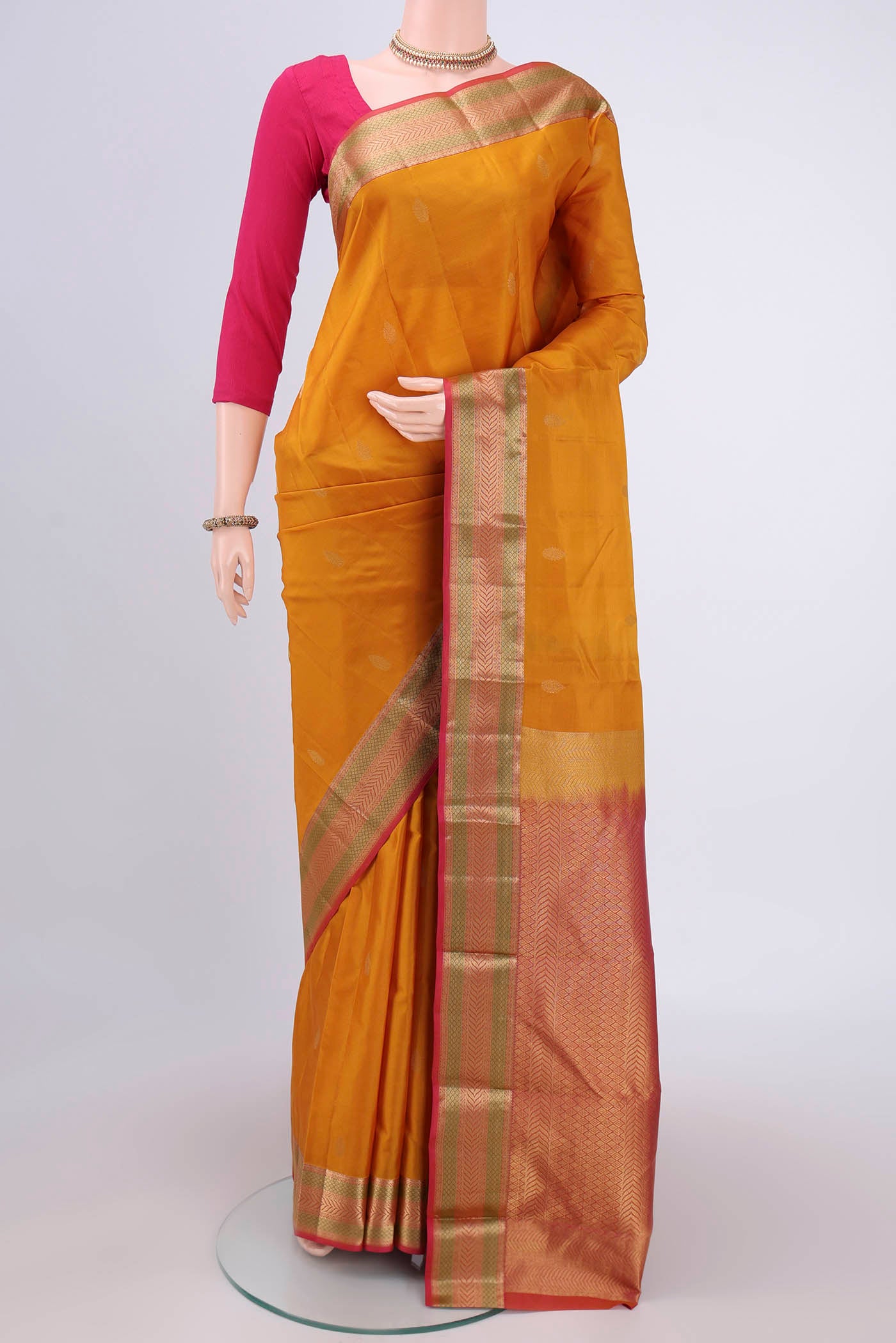 Mustard Kanchipuram Silk Saree with Zari Butta on the body and Zari Border.  displayed on a mannequin