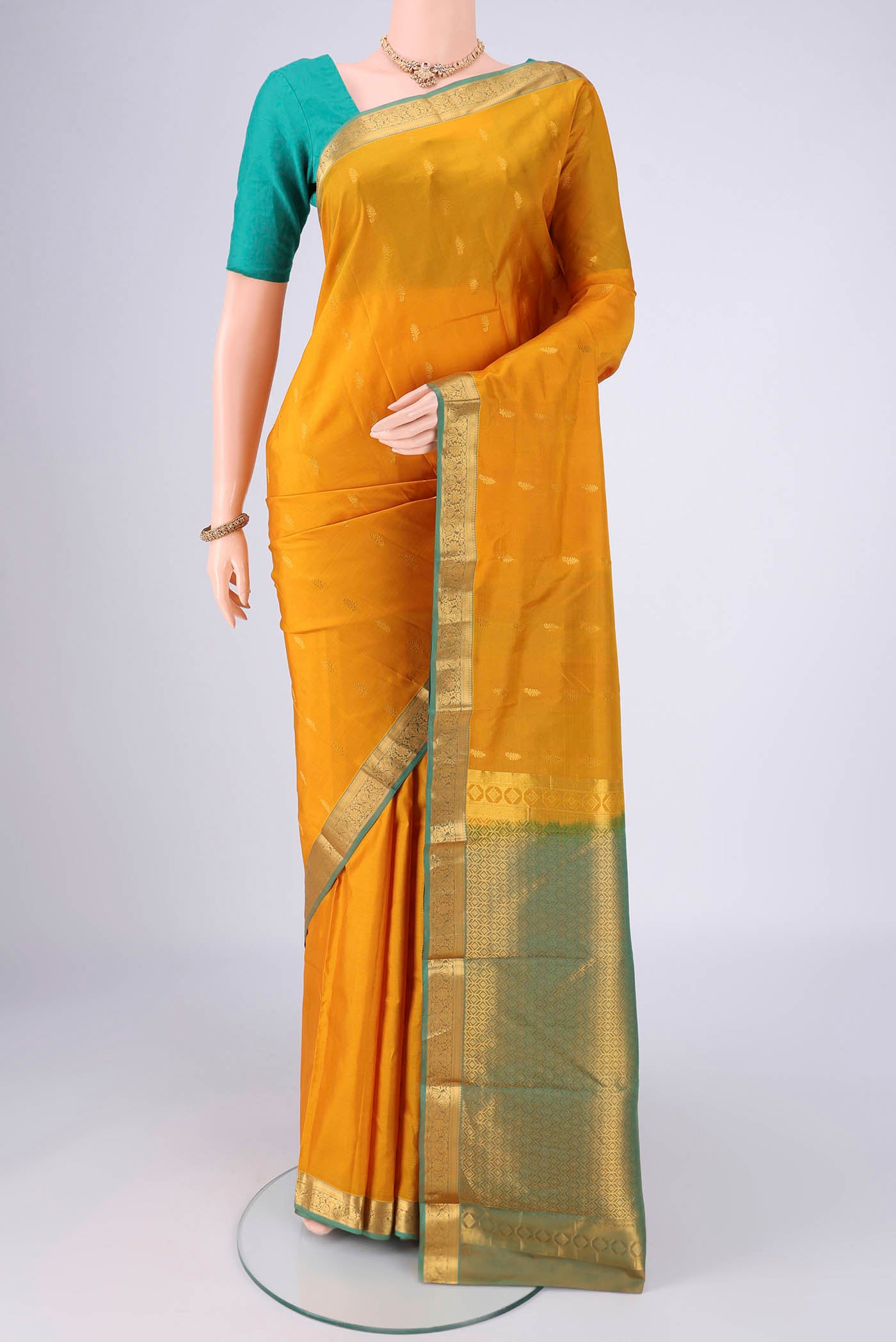Mustard Kanjivaram Silk Saree with Zari Butta on the body and Zari Border.  displayed on a mannequin