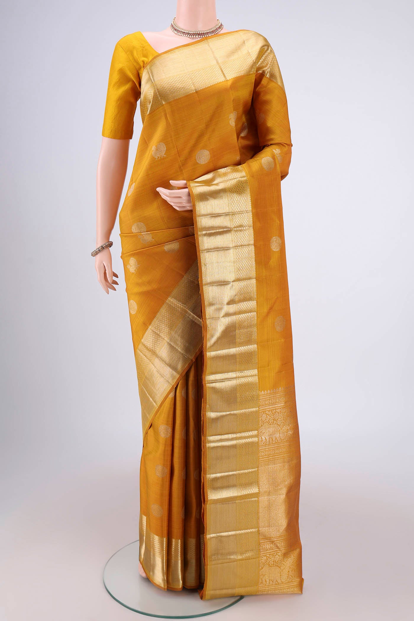 Mustard Kanjivaram Silk Saree with Zari Butta on the body and Zari Border.  displayed on a mannequin