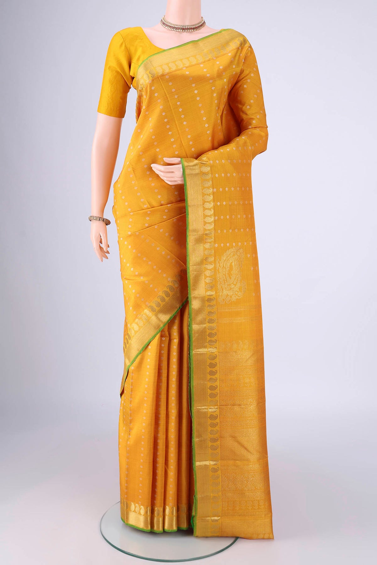 Mustard Kanjivaram Silk Saree with Zari Butta on the body and Zari Border.  displayed on a mannequin