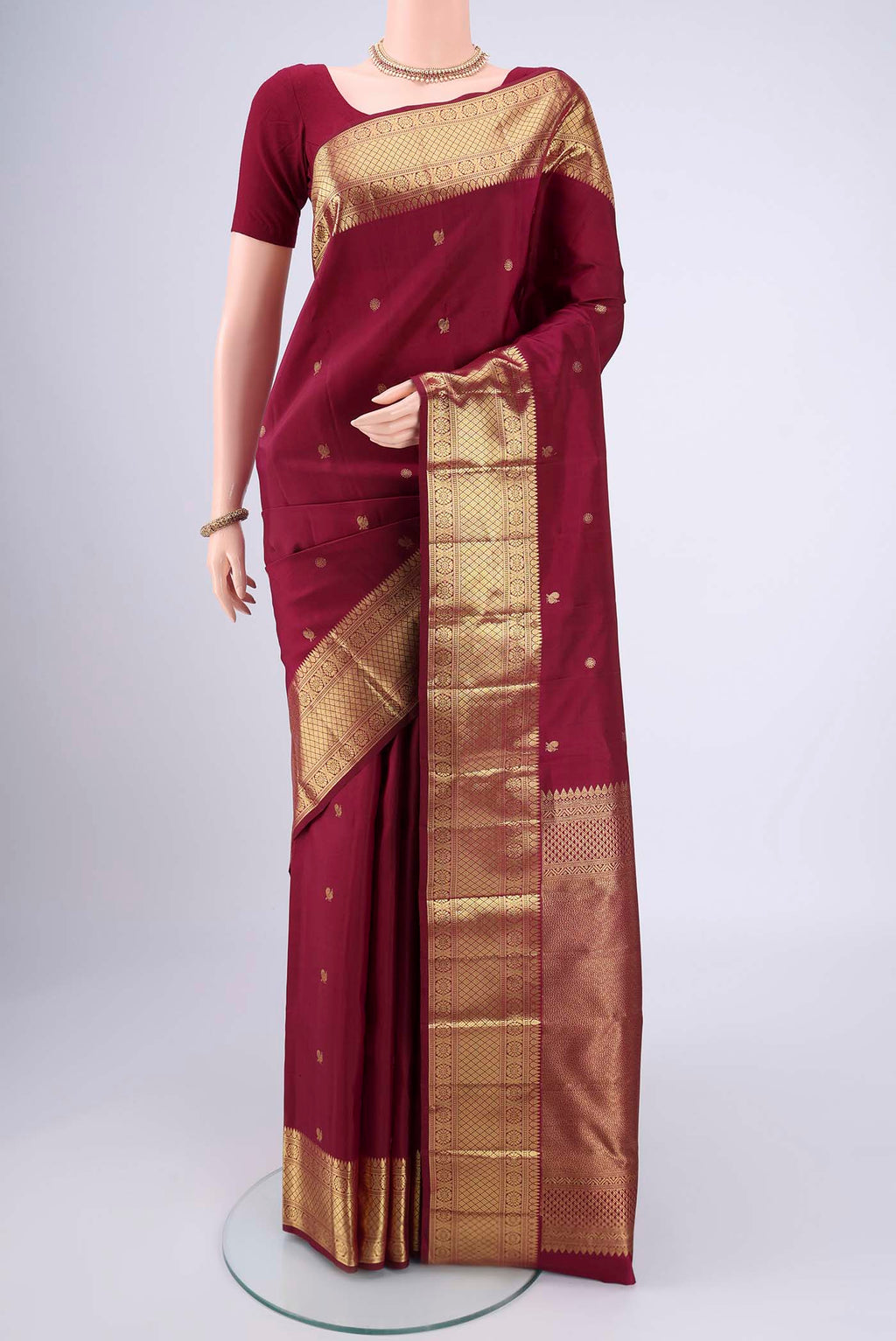 Maroon Kanchipuram Silk Saree with Zari Butta on the body and Zari Border.  displayed on a mannequin