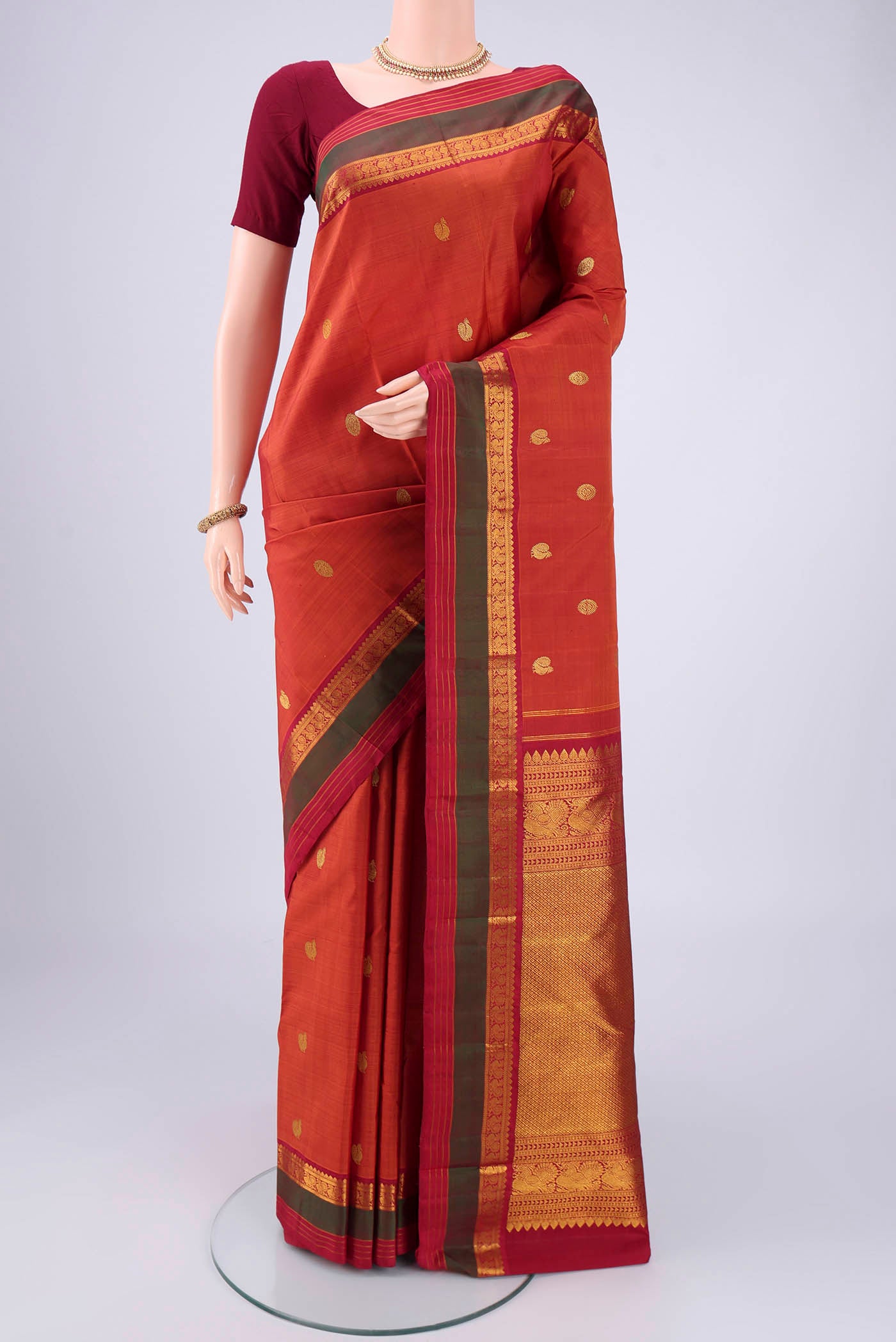 Rust Kanjivaram Silk Saree with Zari Butta on the body and Zari Border.  displayed on a mannequin