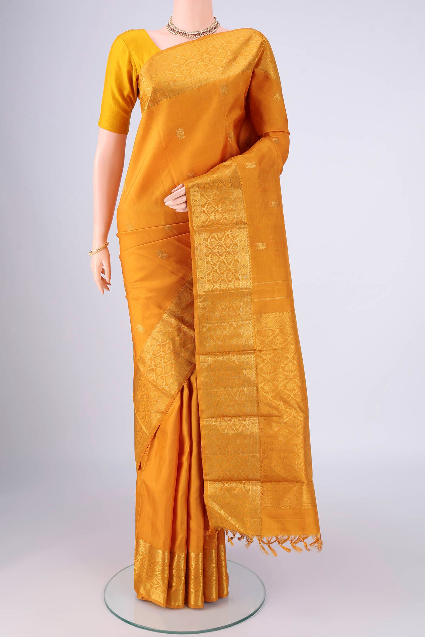 Mustard Kanjivaram Silk Saree with Zari Butta on the body and Zari Border.  displayed on a mannequin