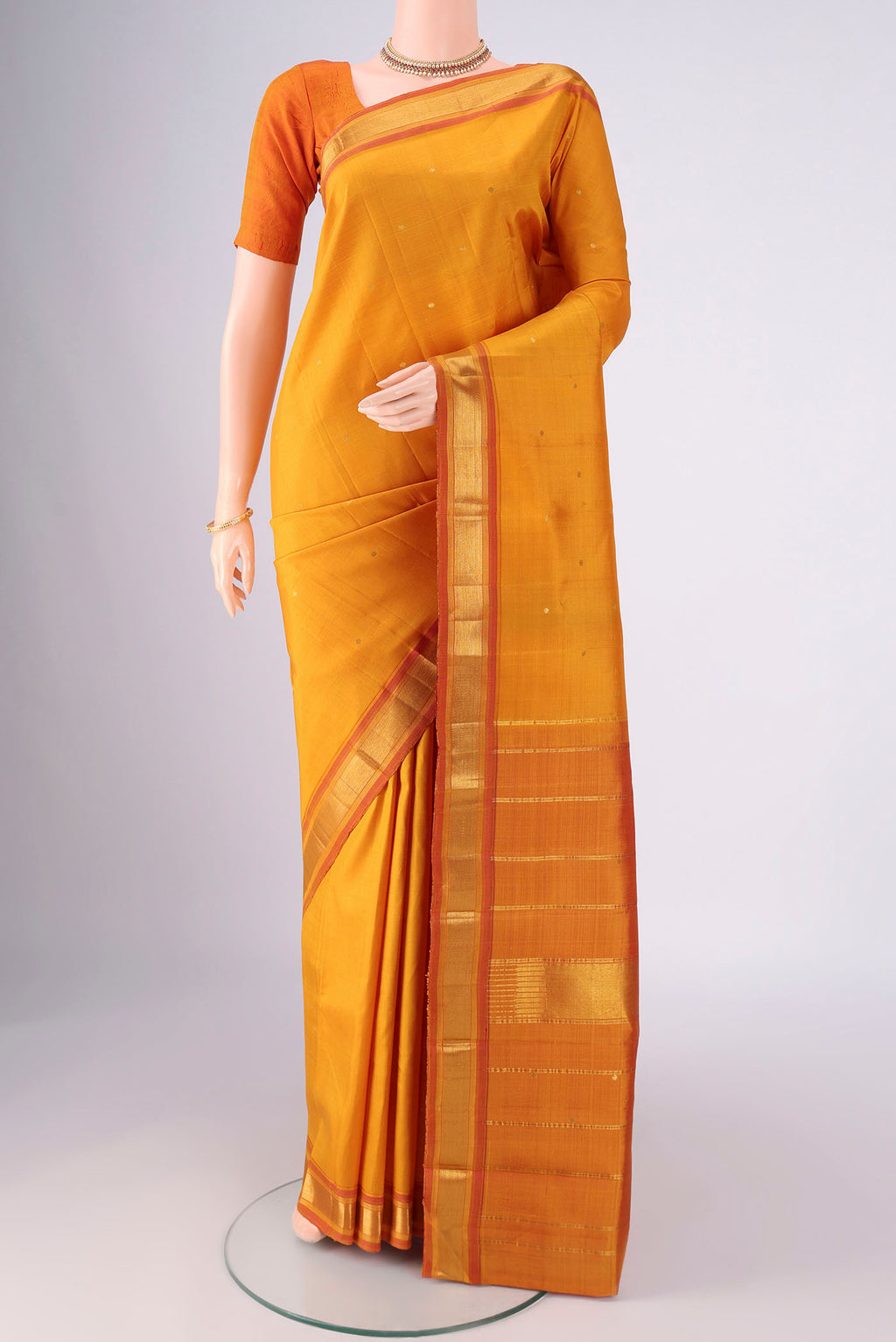 Mustard Kanchipuram Silk Saree with Zari Butta on the body and Zari Border.  displayed on a mannequin