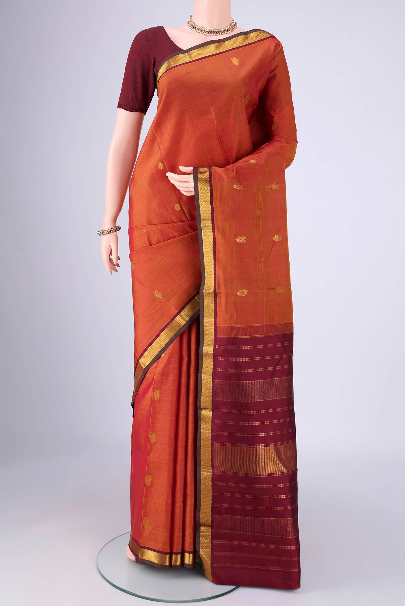 Rust Kanchipuram Silk Saree with Zari Butta on the body and Zari Border.  displayed on a mannequin