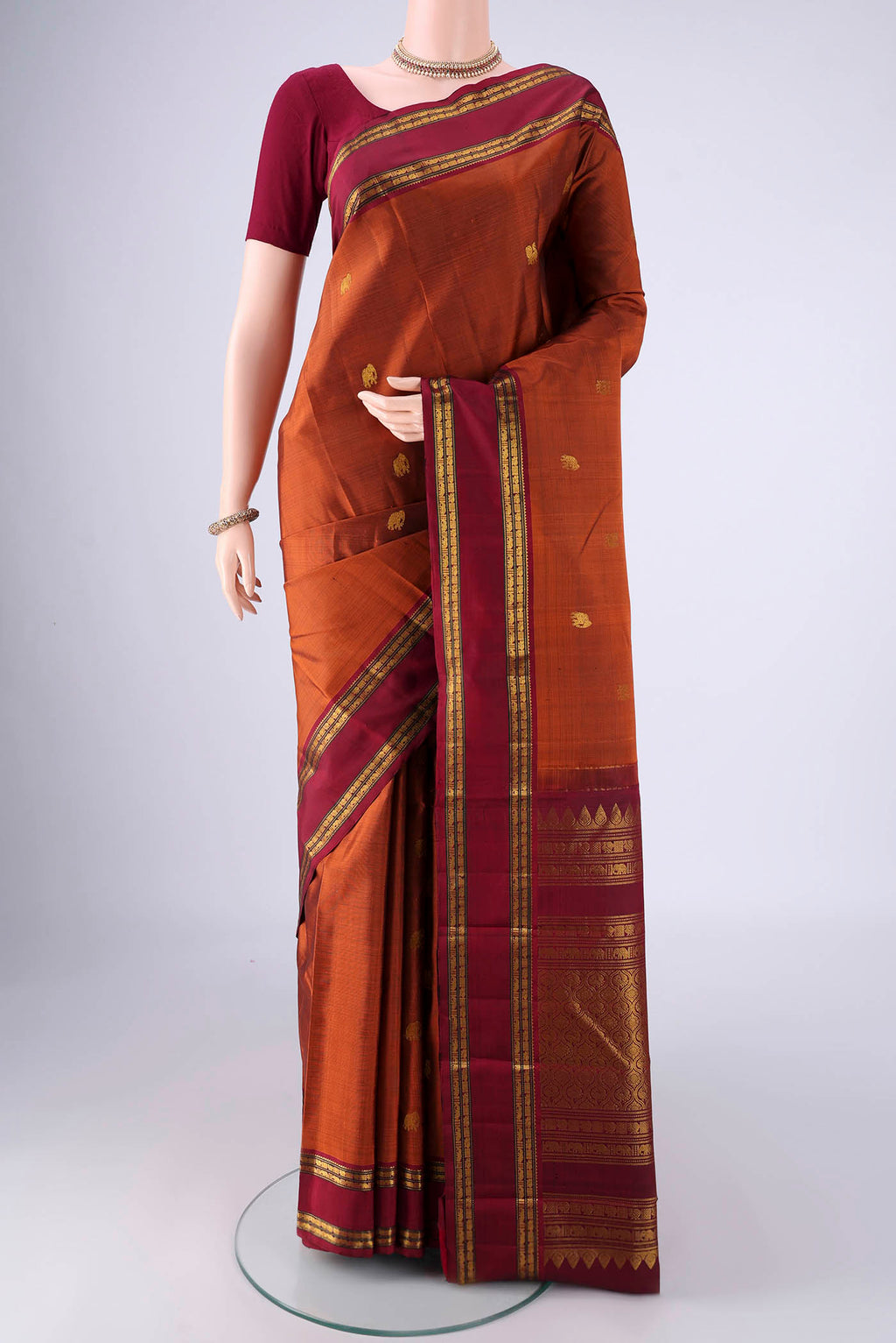 Rust Kanchipuram Silk Saree with Zari Butta on the body and Zari Border.  displayed on a mannequin