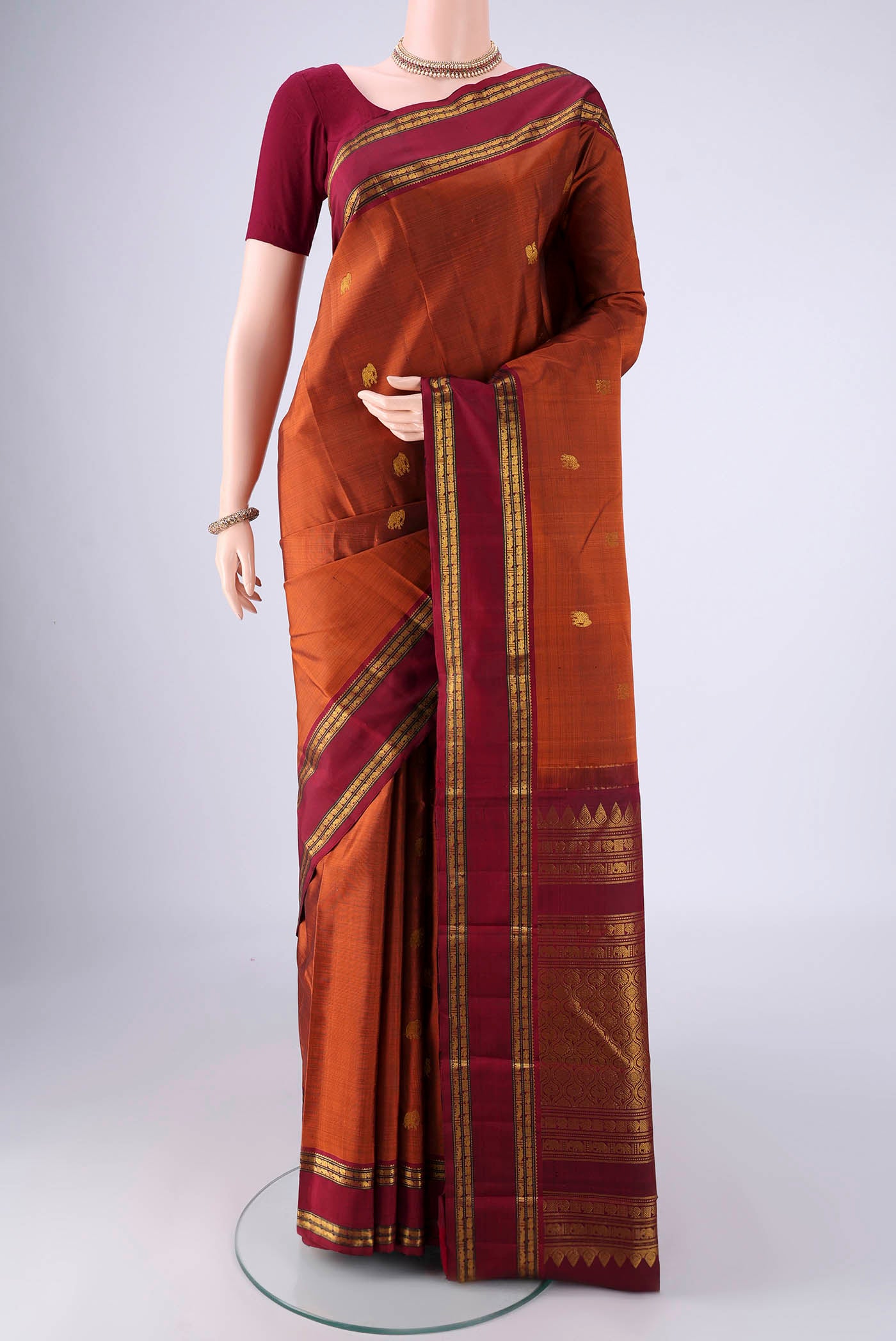 Rust Kanchipuram Silk Saree with Zari Butta on the body and Zari Border.  displayed on a mannequin