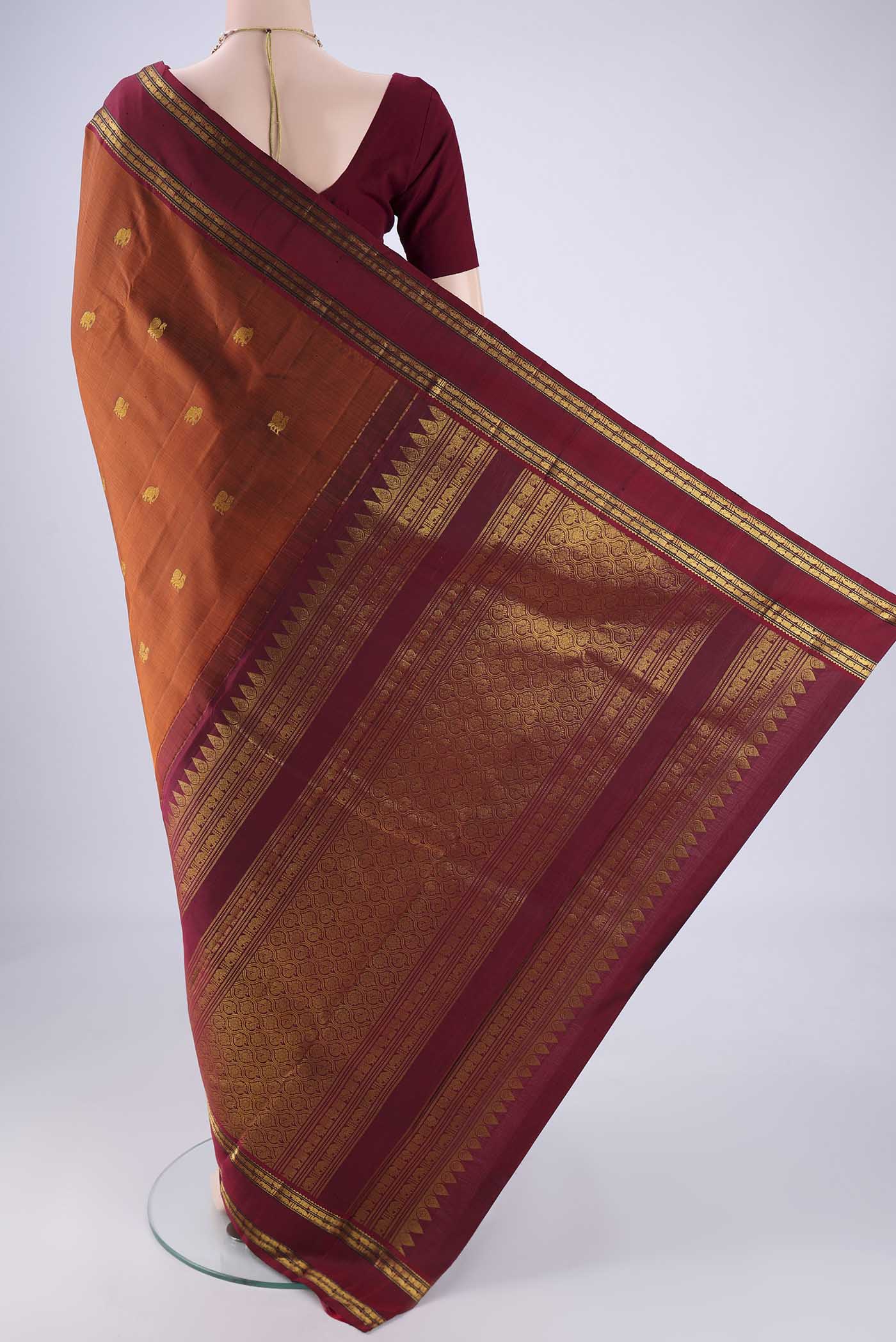 Flat view of Rust Kanchipuram Silk Saree with Zari Butta on the body and Zari Border. 