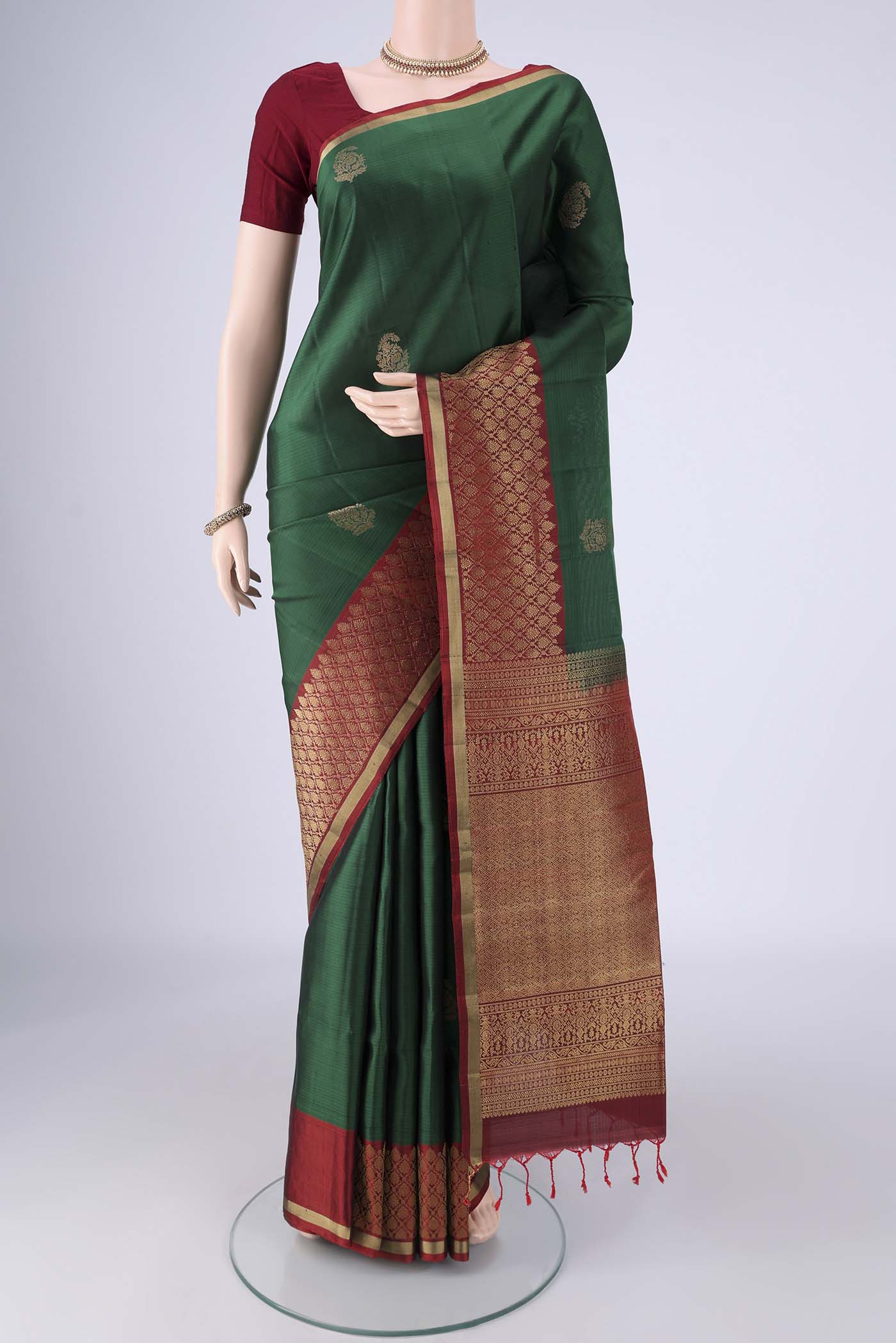 Bottle Green Soft Silk Saree with Zari Butta on the body and Zari Border.  displayed on a mannequin