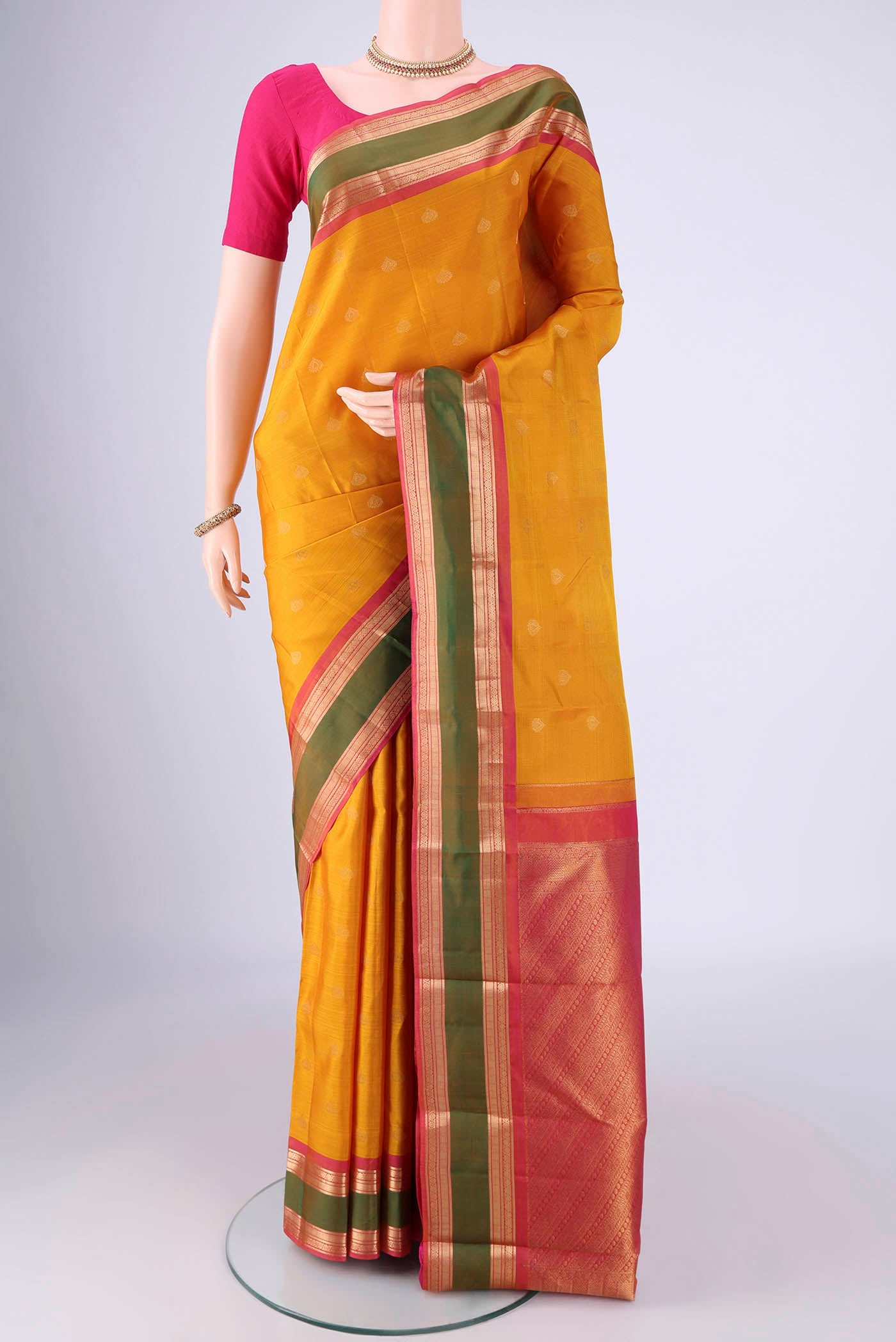 Mustard Kanchipuram Silk Saree with Zari Butta on the body and Zari Border.  displayed on a mannequin