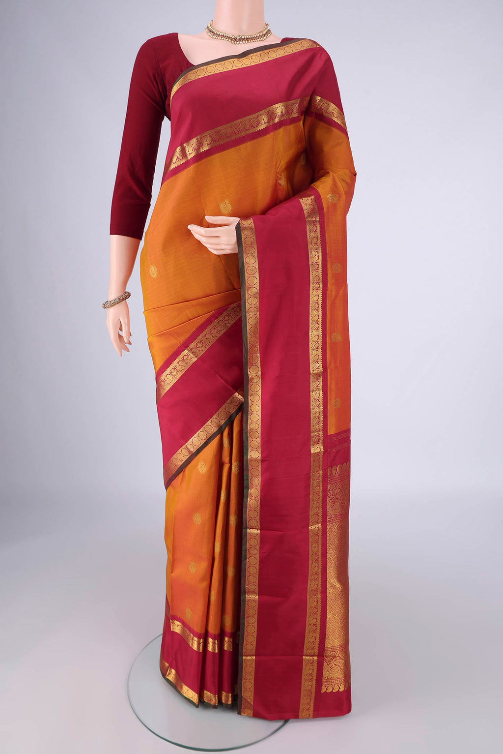 Mustard Kanchipuram Silk Saree with Zari Butta on the body and Zari Border.  displayed on a mannequin