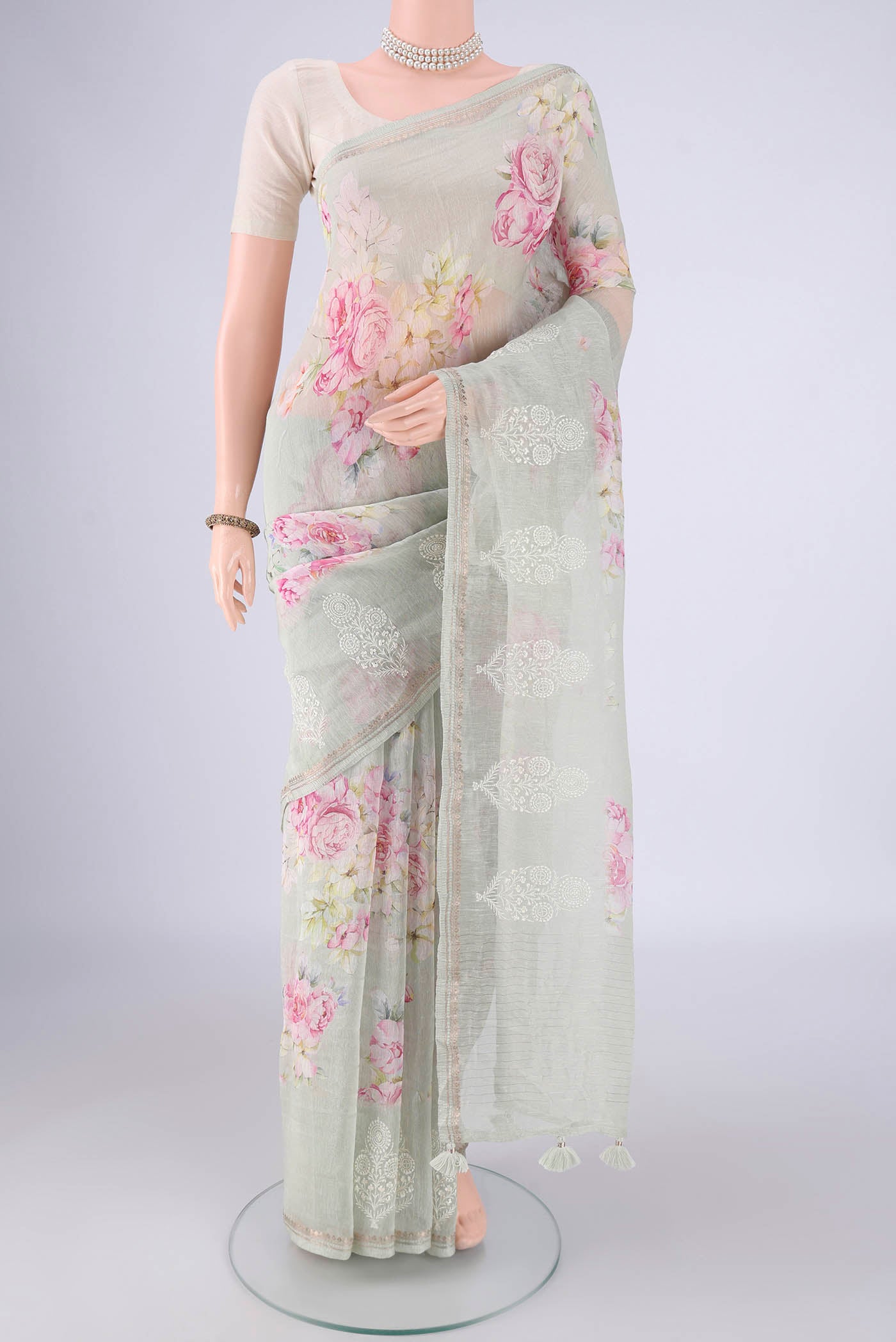 Sage Green Linen Saree with Floral Print on the body and Zari Border.  displayed on a mannequin