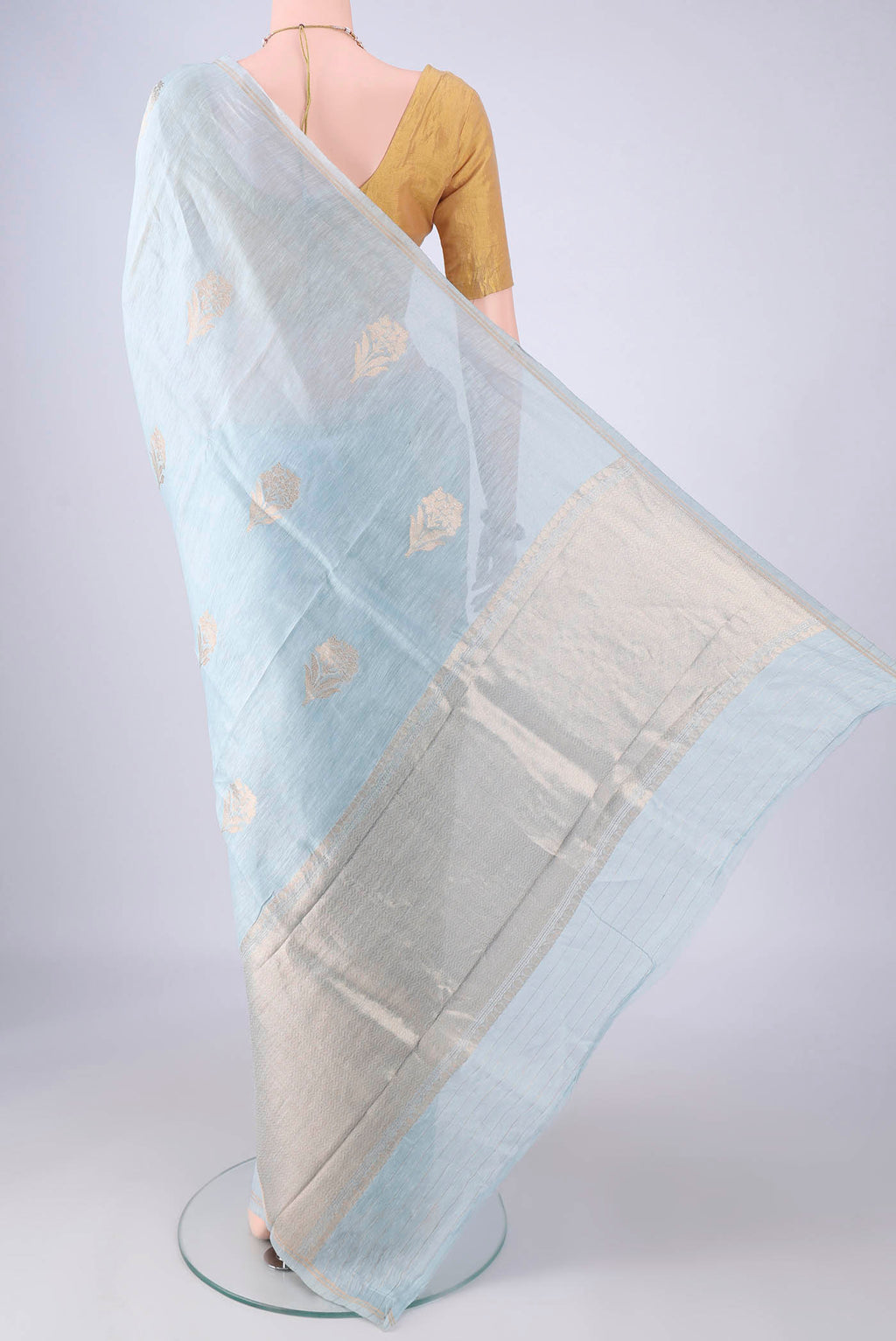 Flat view of Sky Blue Linen Saree with Zari Butta on the body and Thin Zari Line. 