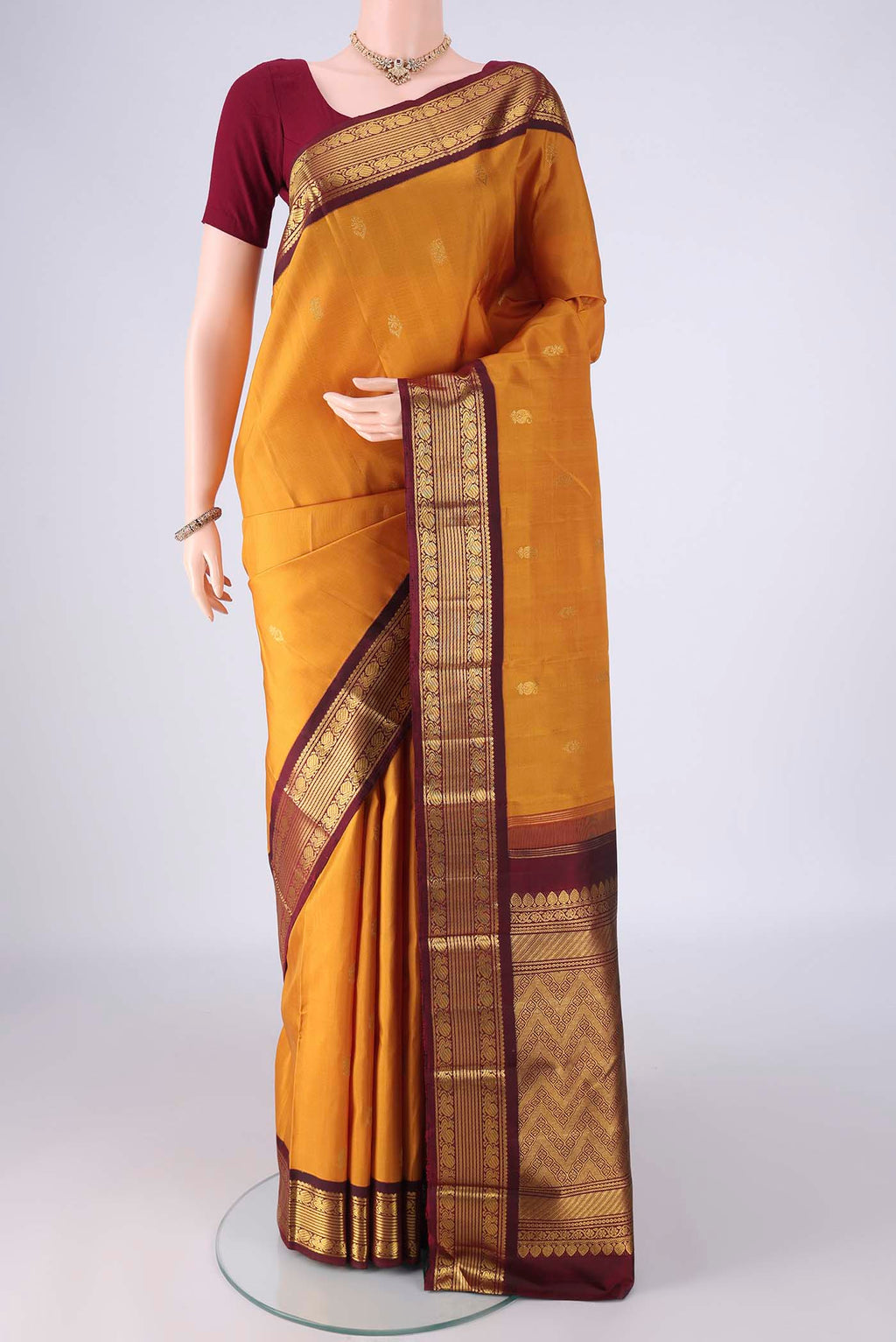 Mustard Kanchipuram Silk Saree with Zari Butta on the body and Zari Border.  displayed on a mannequin