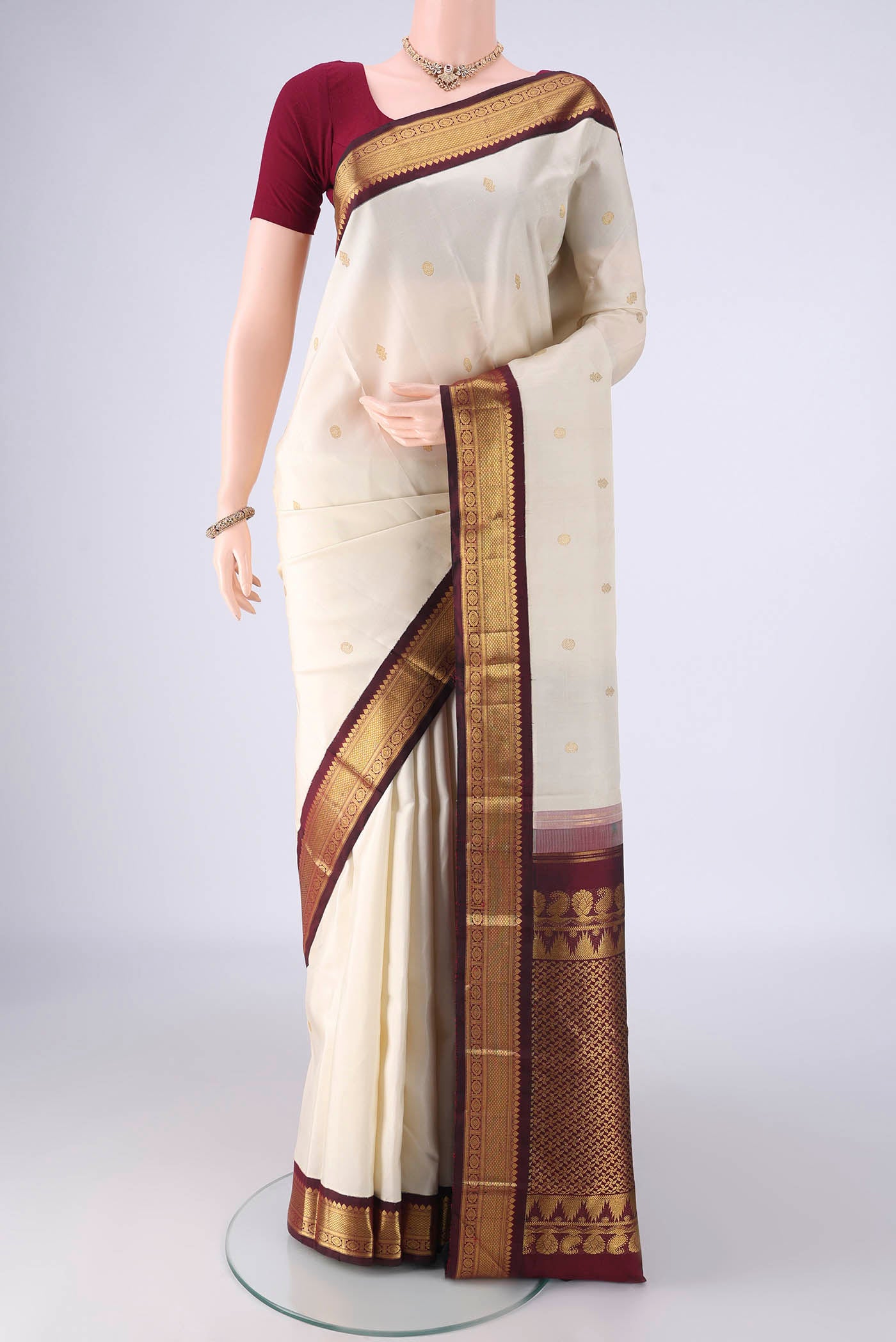 Off White Kanchipuram Silk Saree with Zari Butta on the body and Zari Border.  displayed on a mannequin