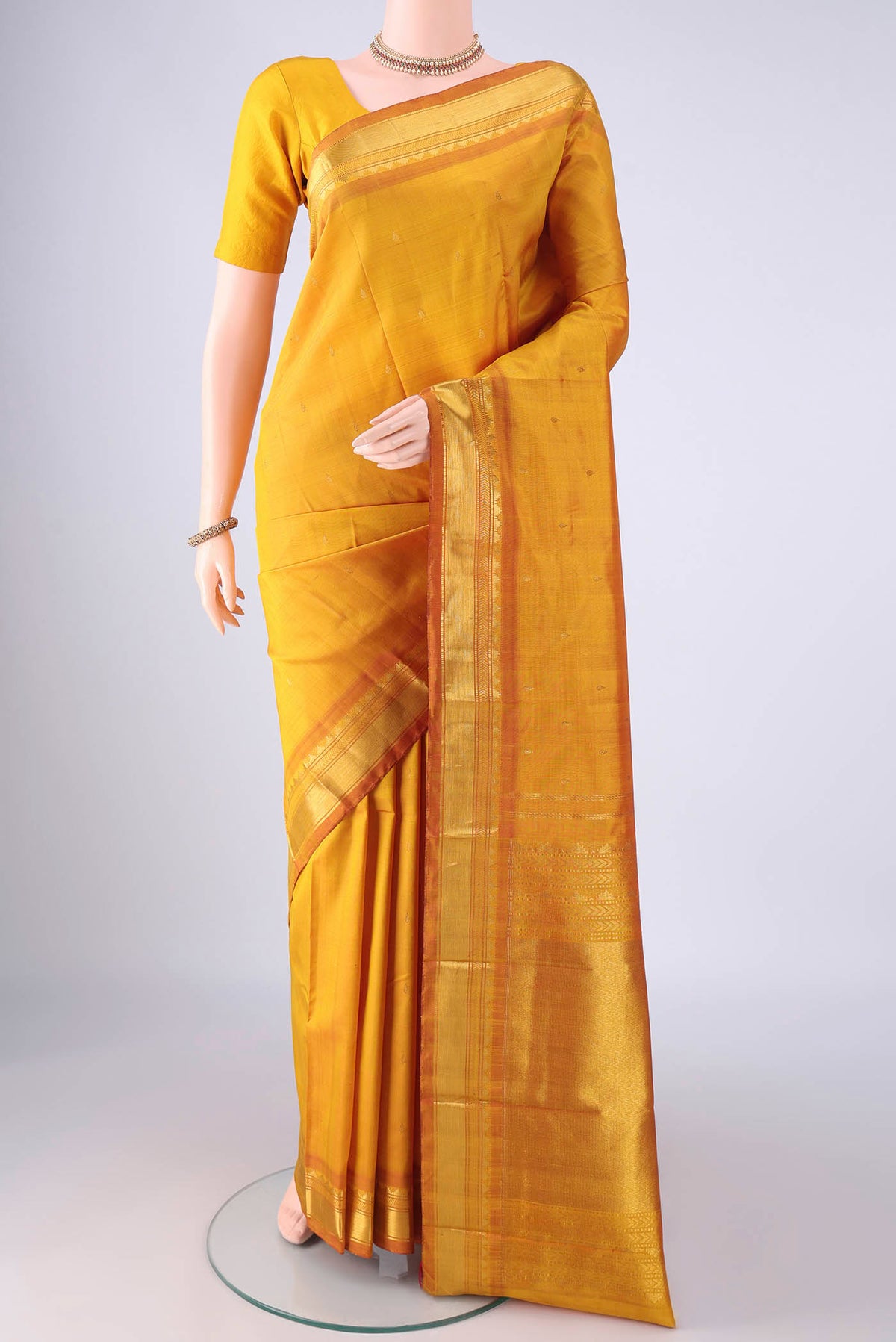 Mustard Kanchipuram Silk Saree with Zari Butta on the body and Zari Border.  displayed on a mannequin