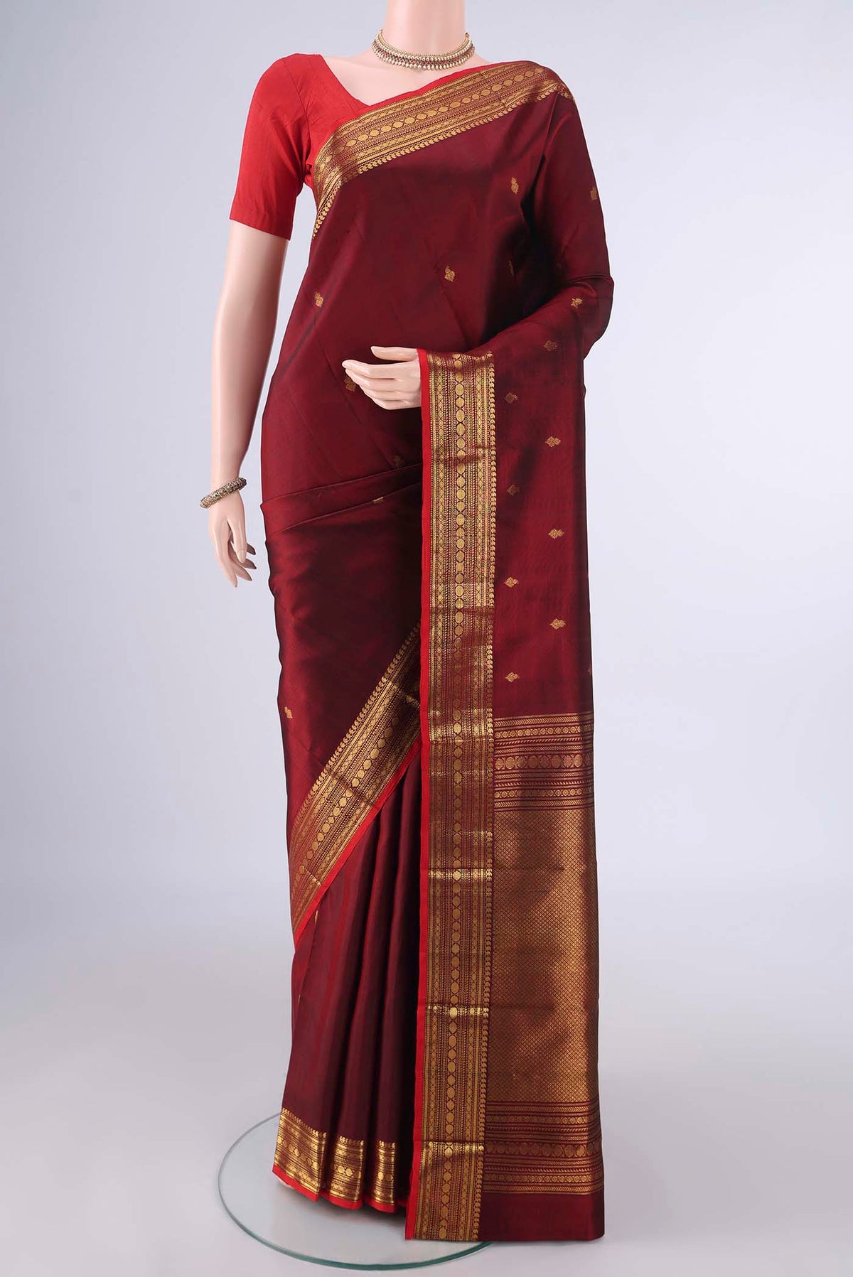 Pure Silk Maroon Kanjivaram Saree with Zari Butta on the body and Zari Border.  displayed on a mannequin