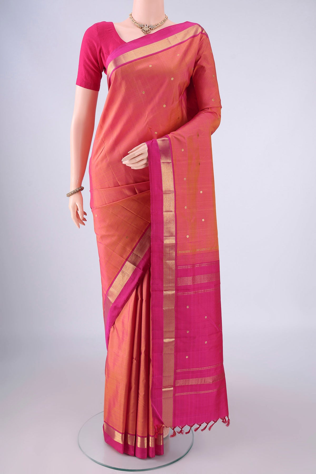 Pinkish Yellow Dual Tone Kanjivaram Silk Saree with Zari Butta on the body and Zari Border.  displayed on a mannequin
