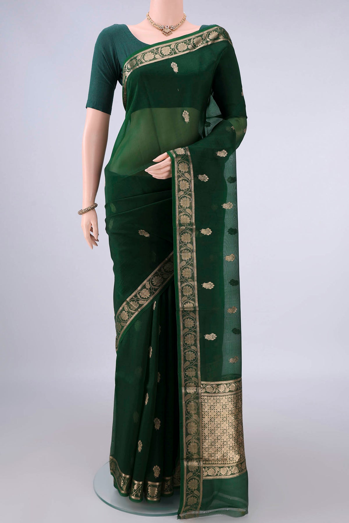 Bottle Green Organza Saree with Zari Butta on the body and Zari Border.  displayed on a mannequin