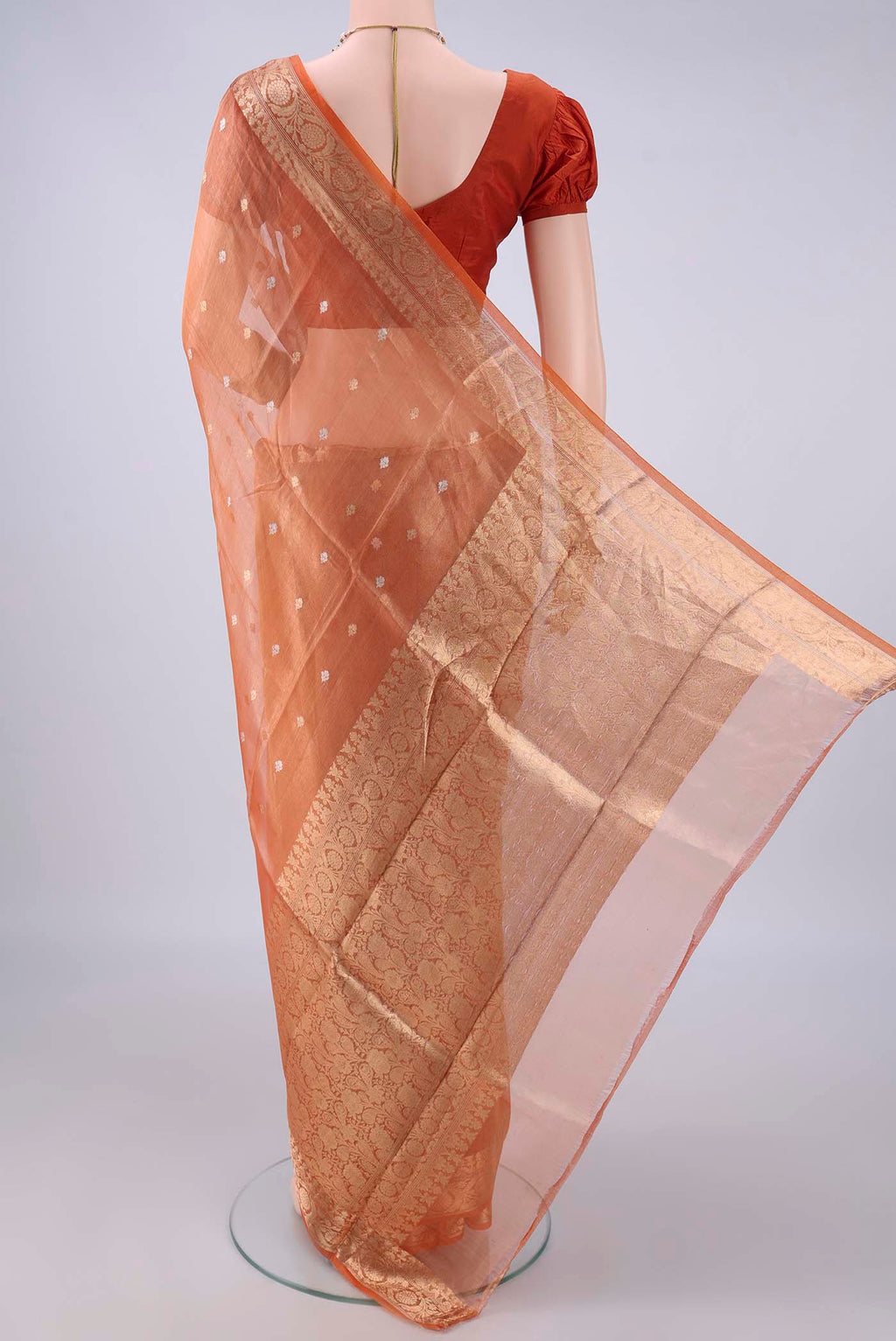 Flat view of Orange Organza Saree with Zari Butta on the body and Zari Border. 