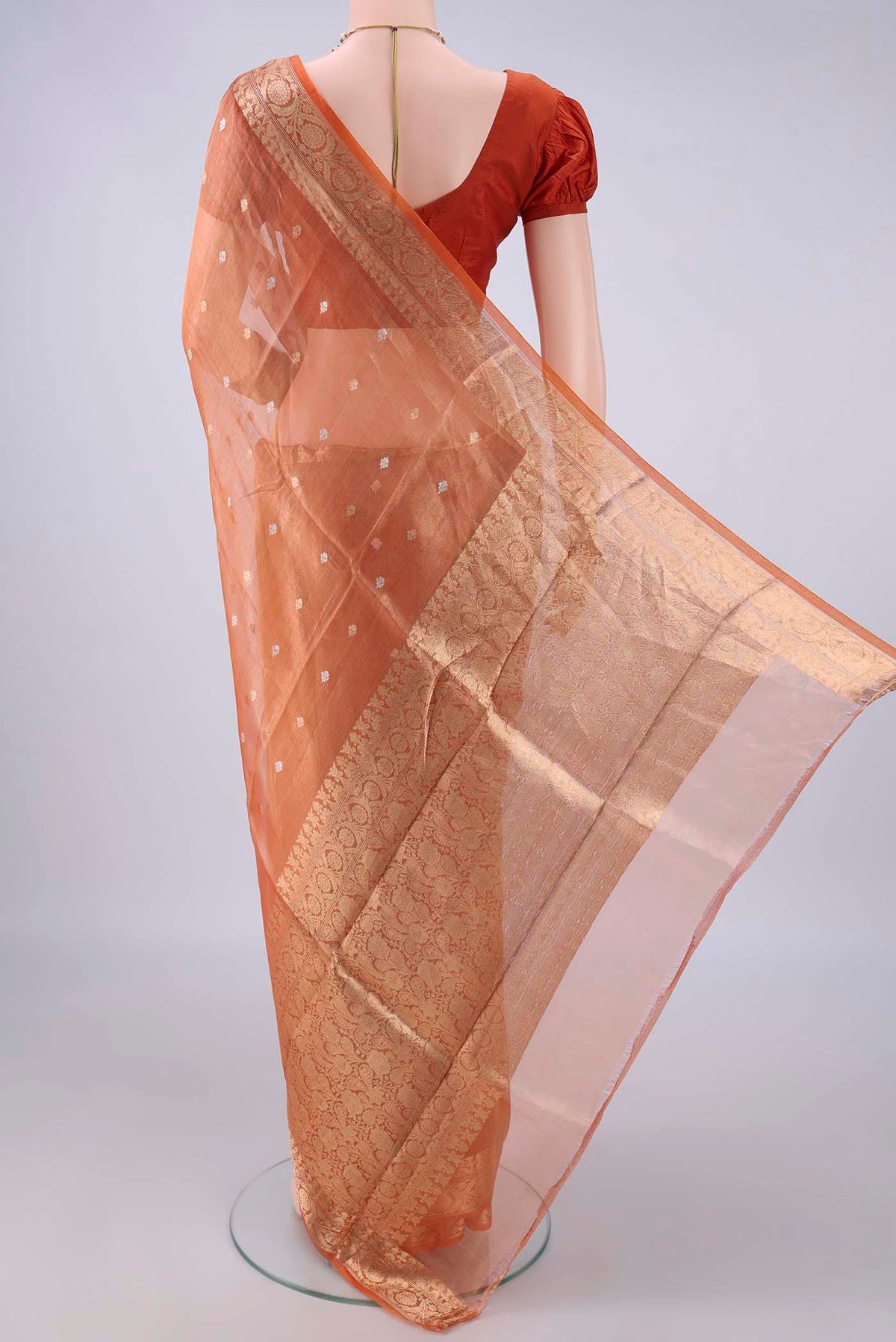 Flat view of Orange Organza Saree with Zari Butta on the body and Zari Border. 