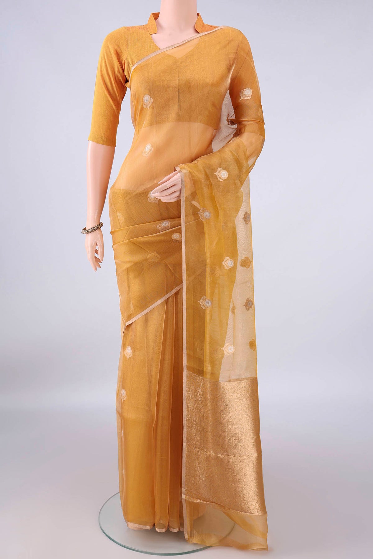 Golden Organza Saree with Zari Butta on the body and Thin Zari Line.  displayed on a mannequin