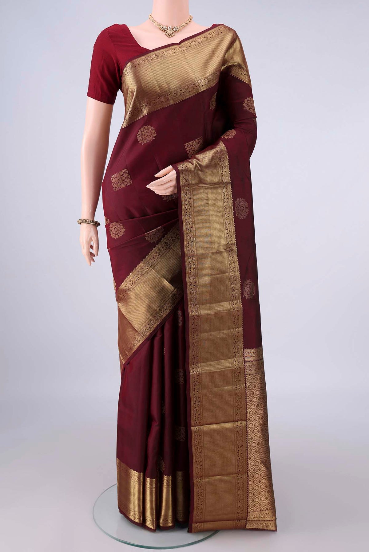 Pure Silk Maroon Kanchipuram Saree with Zari Butta on the body and Zari Border.  displayed on a mannequin
