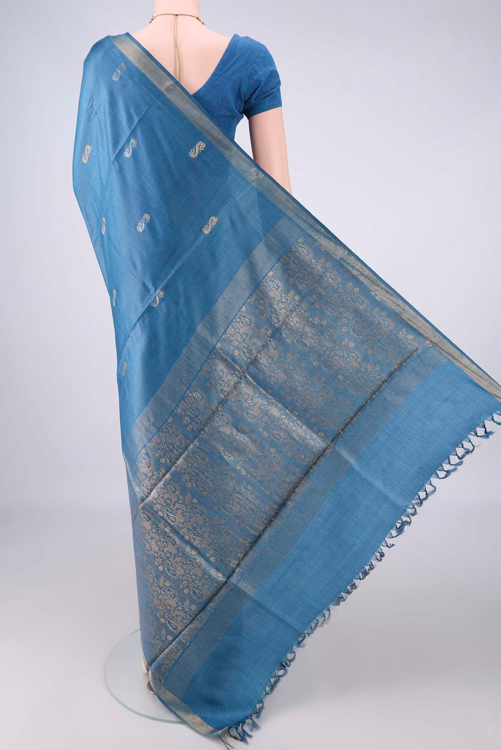 Flat view of Maya Blue Tussar Saree with Zari Butta on the body and Zari Border. 