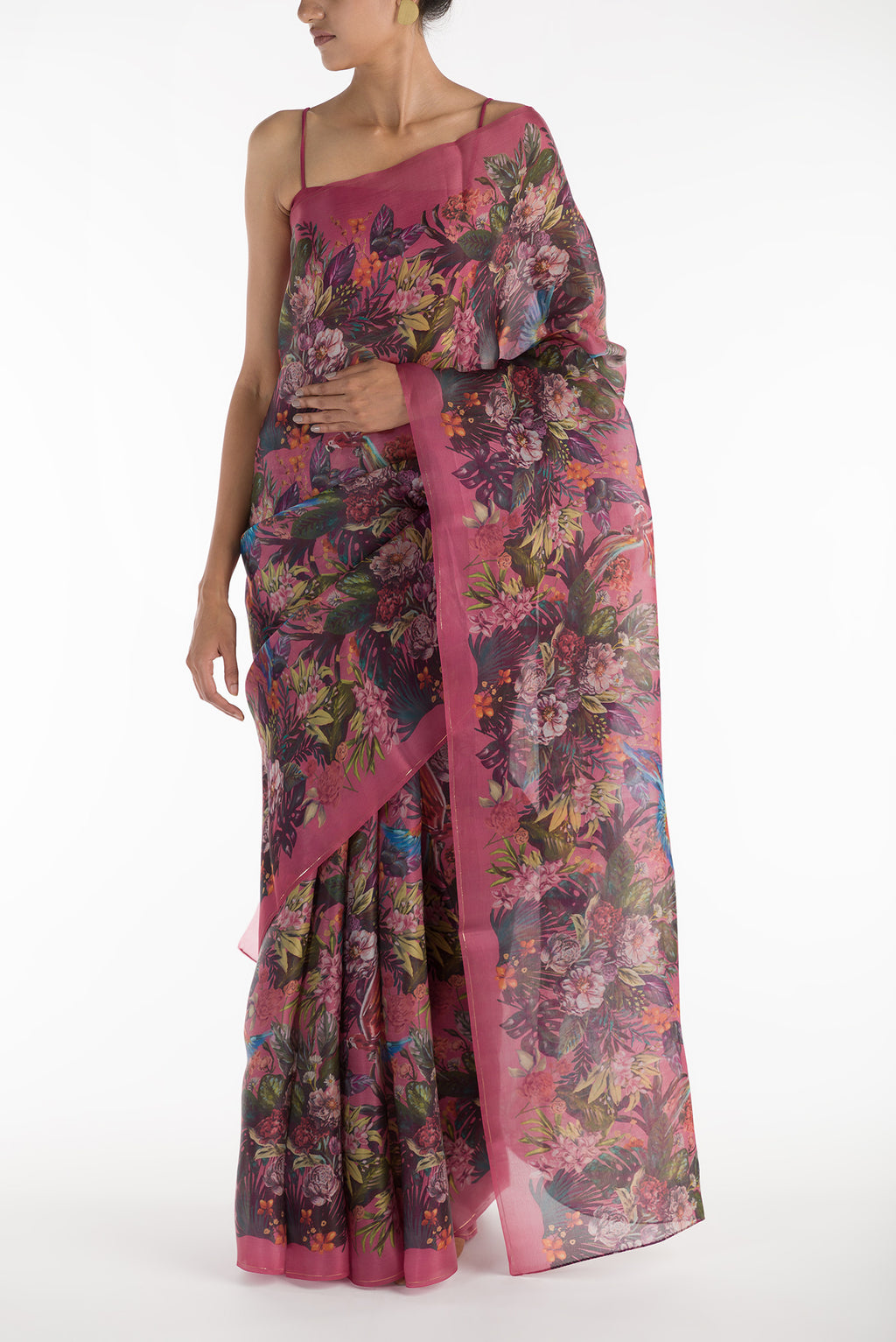 Our 'Hyacinth Macaws' Satin Organza Saree is crafted in a pink tone that features hand-illustrated tropical prints of macaws flying around tropical florals. The saree is completed with the sheen of detailed thin Zari lines. displayed on a mannequin