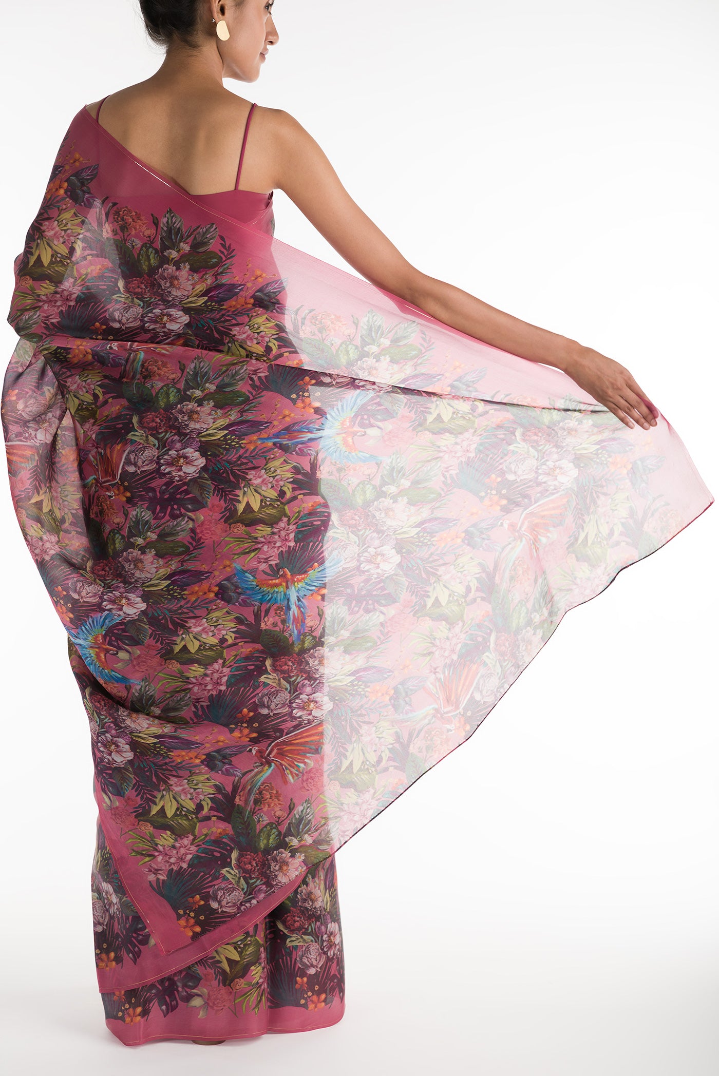 Pleats and pallu of Our 'Hyacinth Macaws' Satin Organza Saree is crafted in a pink tone that features hand-illustrated tropical prints of macaws flying around tropical florals. The saree is completed with the sheen of detailed thin Zari lines.