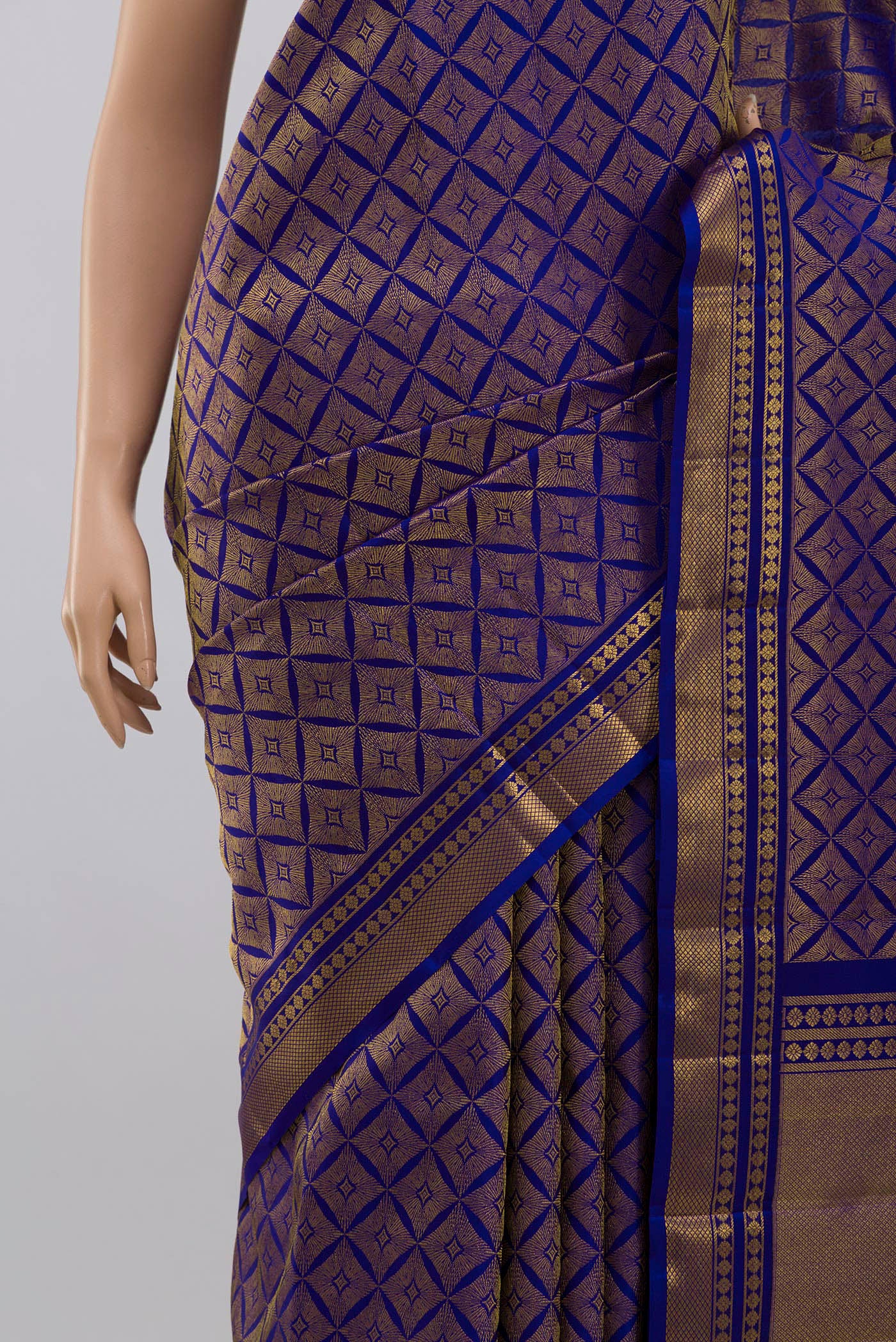 Close up of Handwoven in pure mulberry silk with half-fine gold and silver zari, this blue Kanjeevaram saree celebrates the harmony of line and light. A refined checkered pattern, formed by intersecting gold zari lines, unfolds across the body and continues into the radiant gold pallu. Framed by two broad gold bands separated by a slender gold stripe, the border lends the weave timeless balance and elegance. displaying folds