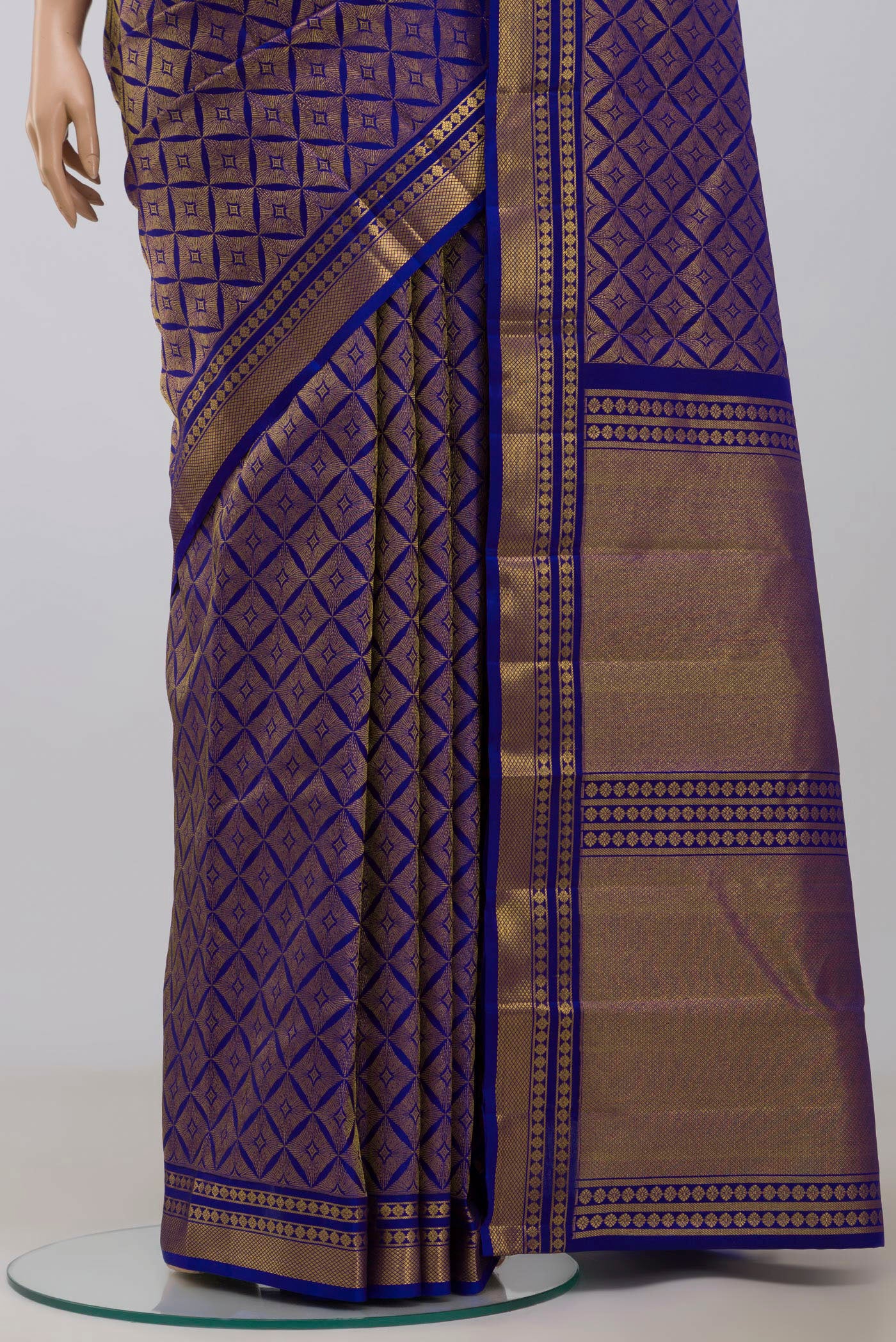 Pleats and pallu of Handwoven in pure mulberry silk with half-fine gold and silver zari, this blue Kanjeevaram saree celebrates the harmony of line and light. A refined checkered pattern, formed by intersecting gold zari lines, unfolds across the body and continues into the radiant gold pallu. Framed by two broad gold bands separated by a slender gold stripe, the border lends the weave timeless balance and elegance.