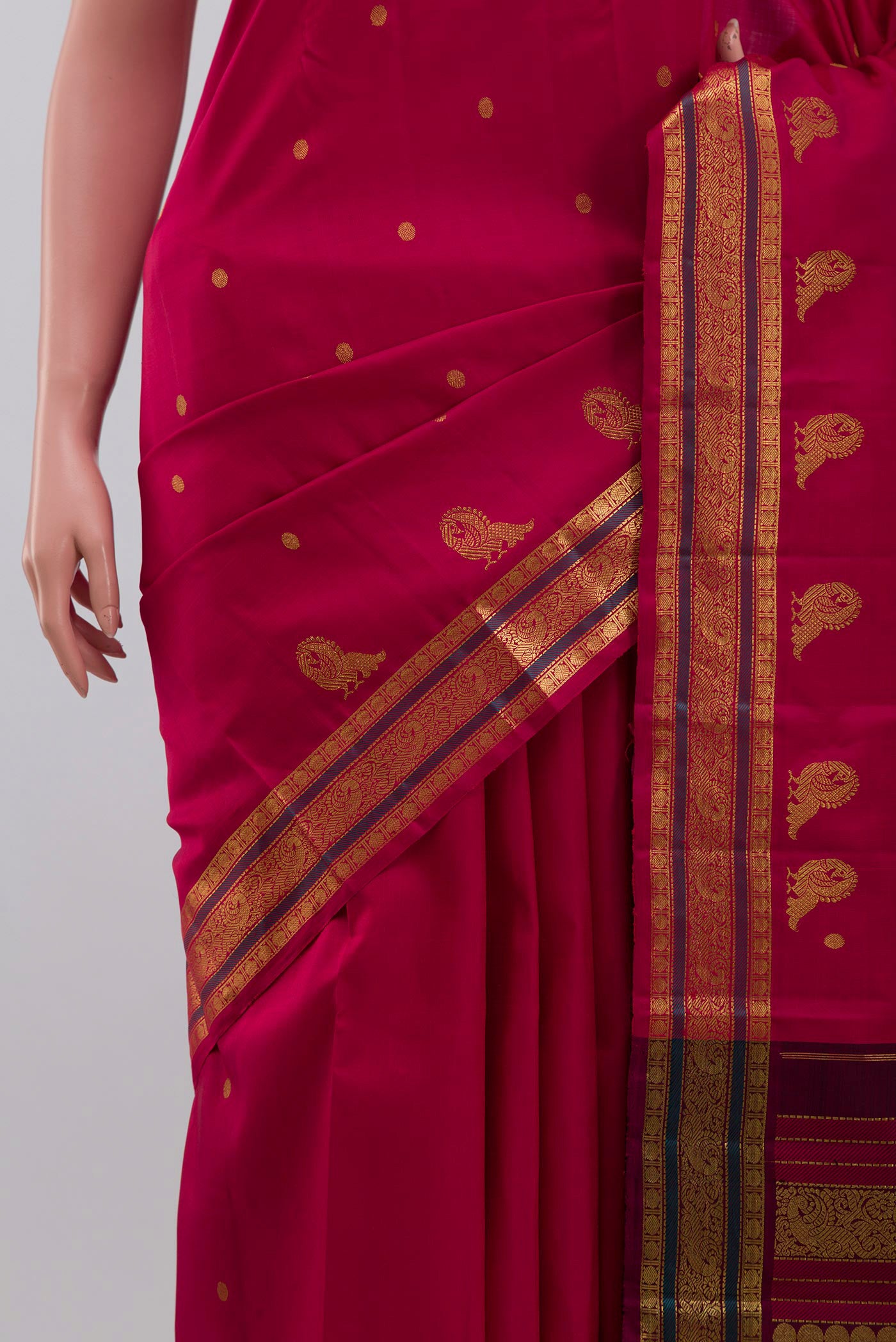 Close up of Aaradhya unfolds in a vibrant scarlet red, adorned with delicate rudraksh butas that bring depth and rhythm to the weave. The 3-inch borders feature mayil zari pet and rudraksh pet framed by contrasting silk bands. Along the lower border, graceful mayils with unfurled wings create a striking visual detail. The pallu is highlighted by a distinctive grid pattern accented with vibrant green bands displaying folds
