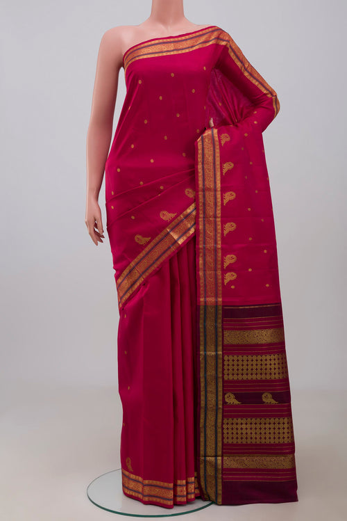 Aaradhya unfolds in a vibrant scarlet red, adorned with delicate rudraksh butas that bring depth and rhythm to the weave. The 3-inch borders feature mayil zari pet and rudraksh pet framed by contrasting silk bands. Along the lower border, graceful mayils with unfurled wings create a striking visual detail. The pallu is highlighted by a distinctive grid pattern accented with vibrant green bands displayed on a mannequin