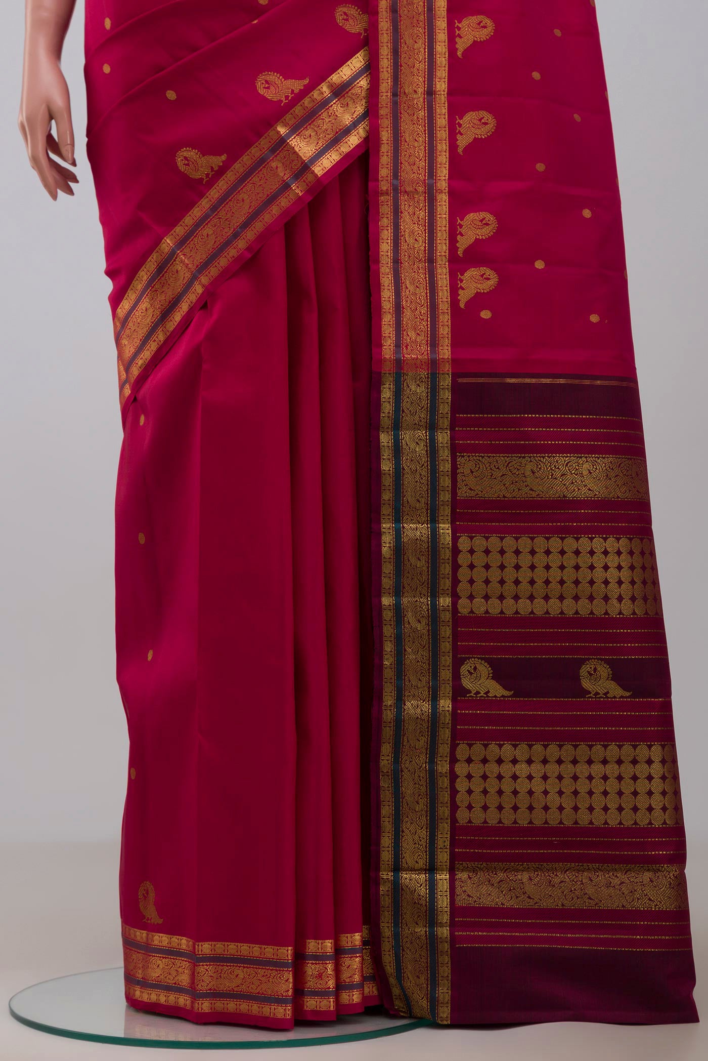 Pleats and pallu of Aaradhya unfolds in a vibrant scarlet red, adorned with delicate rudraksh butas that bring depth and rhythm to the weave. The 3-inch borders feature mayil zari pet and rudraksh pet framed by contrasting silk bands. Along the lower border, graceful mayils with unfurled wings create a striking visual detail. The pallu is highlighted by a distinctive grid pattern accented with vibrant green bands