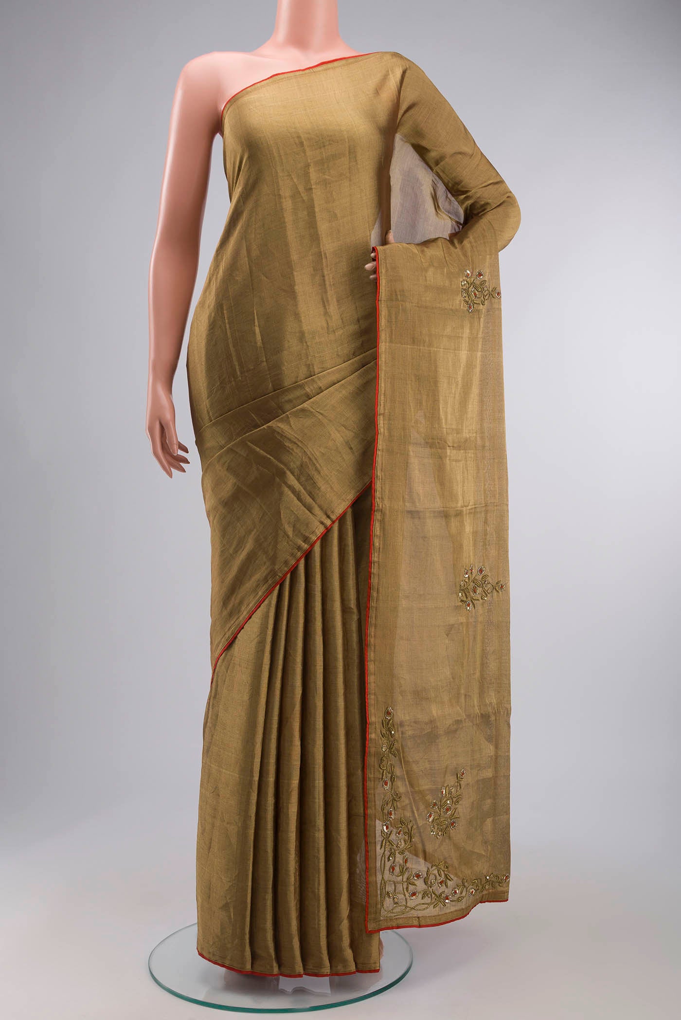 Rumana is crafted in delicate tissue enriched with antique-gold zardozi, brought to life through dabka, sequins, and coloured beads The pallu unfolds with konia motifs and flowing pomegranate vines, anchored by a drop-shaped buta rendered in a stylised pomegranate form The body carries evenly placed butas that continue into the pleats, lending the saree a gentle, composed rhythm A classic gota trim completes this elegant expression of symbolic craft displayed on a mannequin