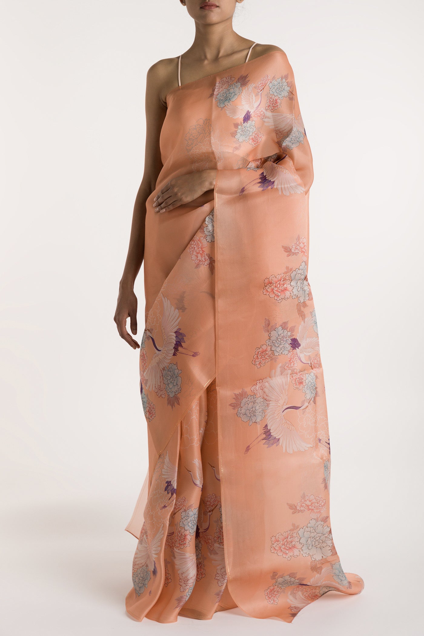 Our 'Flying Cranes' printed on a satin organza saree is crafted in a peach tone that features hand-illustrated tropical prints of flying cranes in the endless sky. The saree is finished with an intricately detailed thin Zari line along the border. displayed on a mannequin